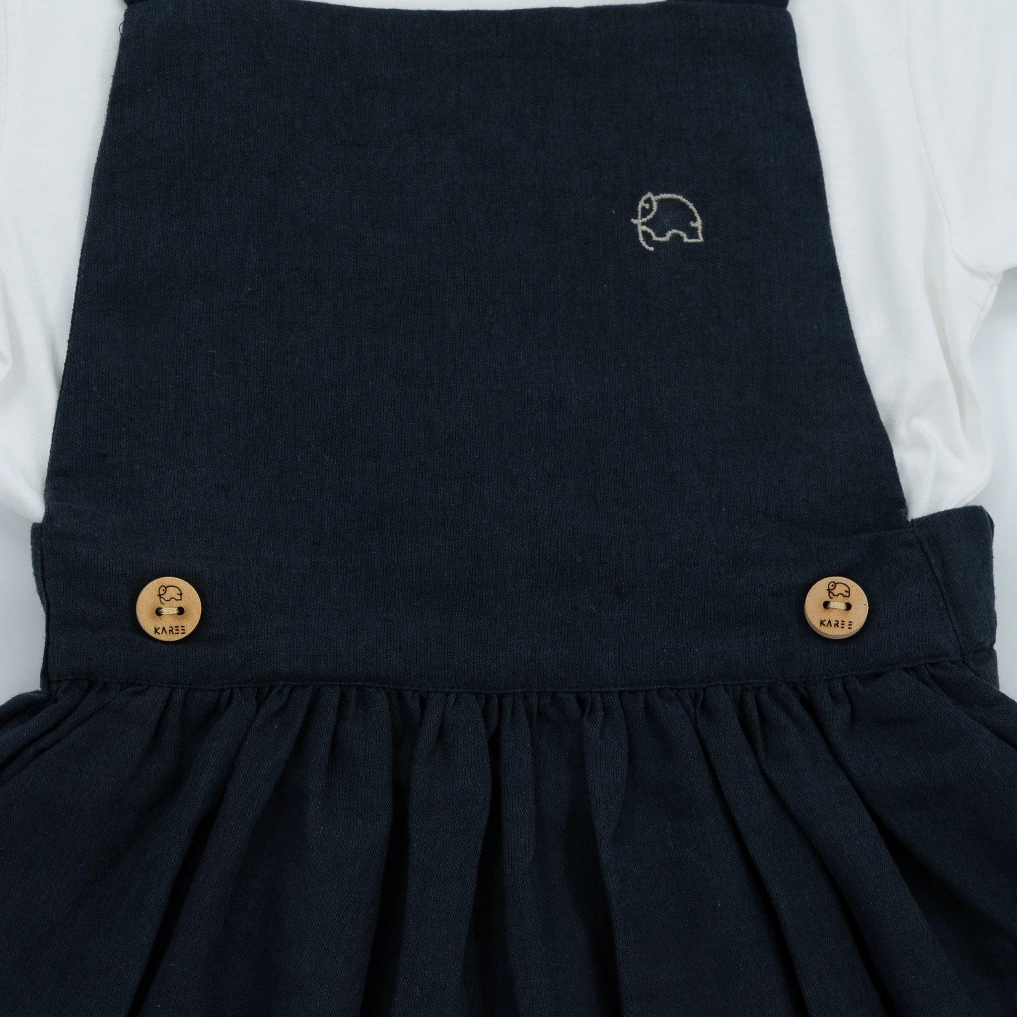 Close-up of an Ebony Black Linen Pinafore for Girls from Karee with two wooden buttons and a small white embroidered logo on the front, exemplifying timeless sophistication.