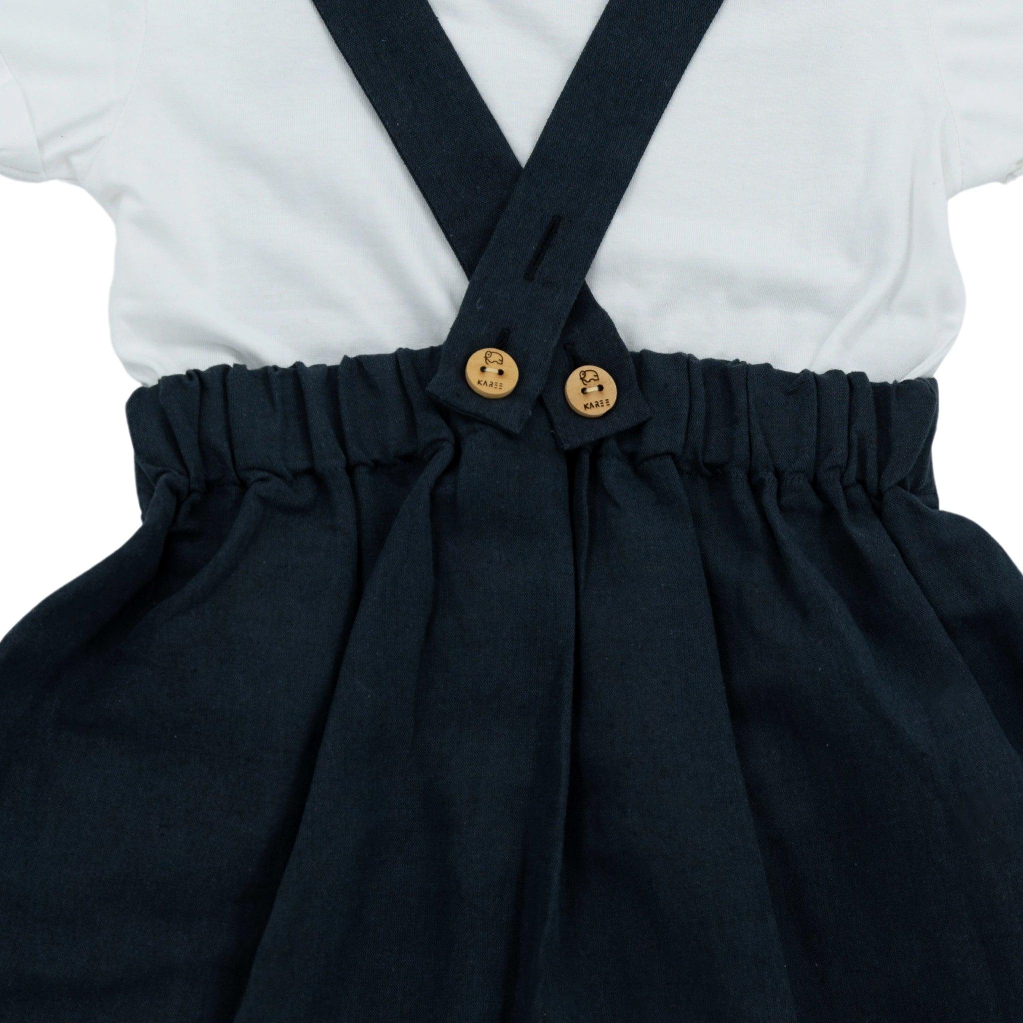 Close-up of a child's Karee Ebony Black Linen Pinafore for Girls attached to a gathered waist skirt, featuring wooden buttons, against a white shirt background.