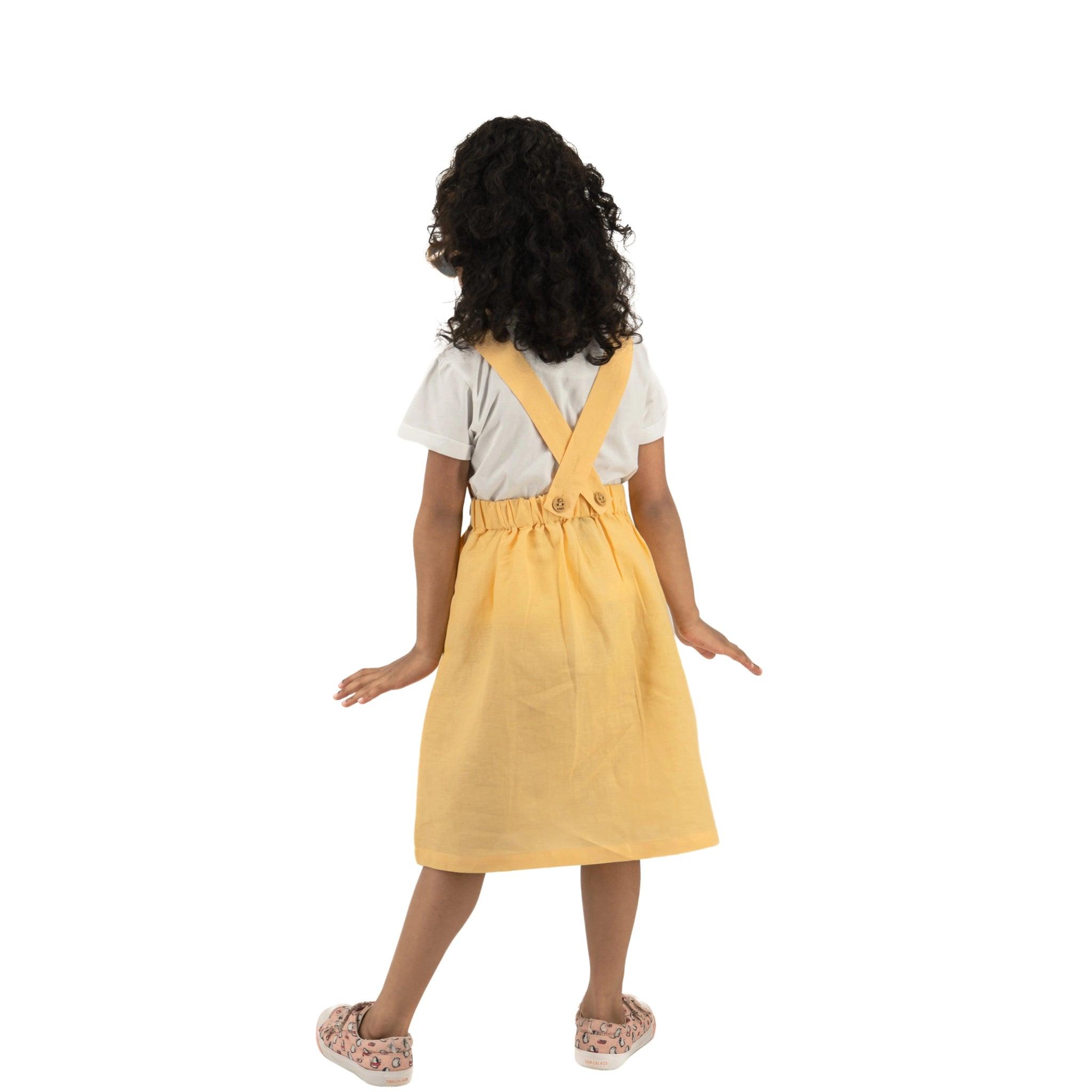 A young girl in a yellow Golden Fleece Linen Pinafore and white shirt walks away, viewed from behind, against a white background.