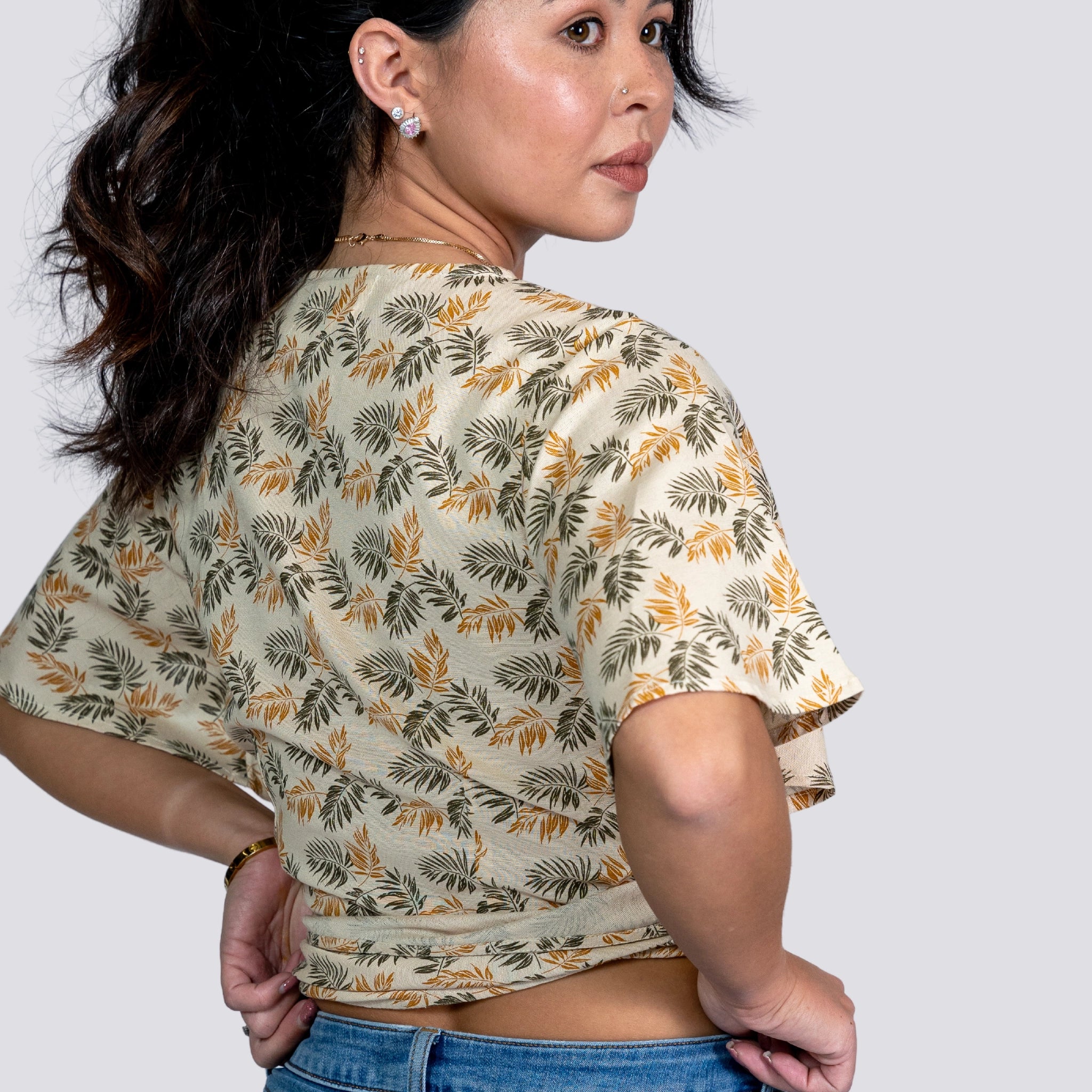 Woman in a ChicPalms Women's Eco-Friendly Wrap Top - Biscuit Bliss and jeans looking over her shoulder against a grey background.