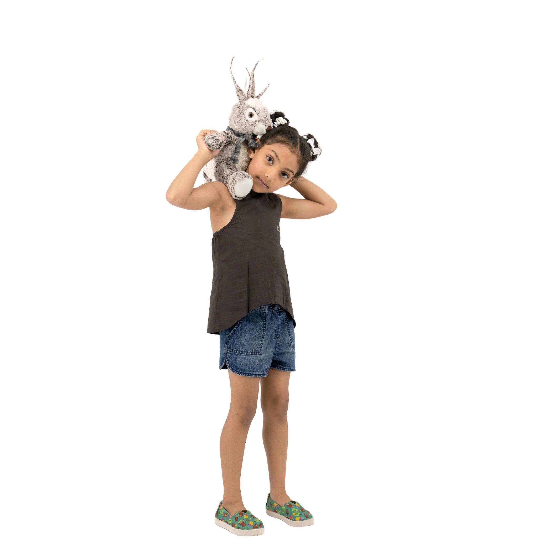 A young girl with pigtails, wearing a Karee Plum Kitten Cotton Bib Neck Top for Kids and denim shorts, playfully holds a stuffed rabbit on her shoulder.