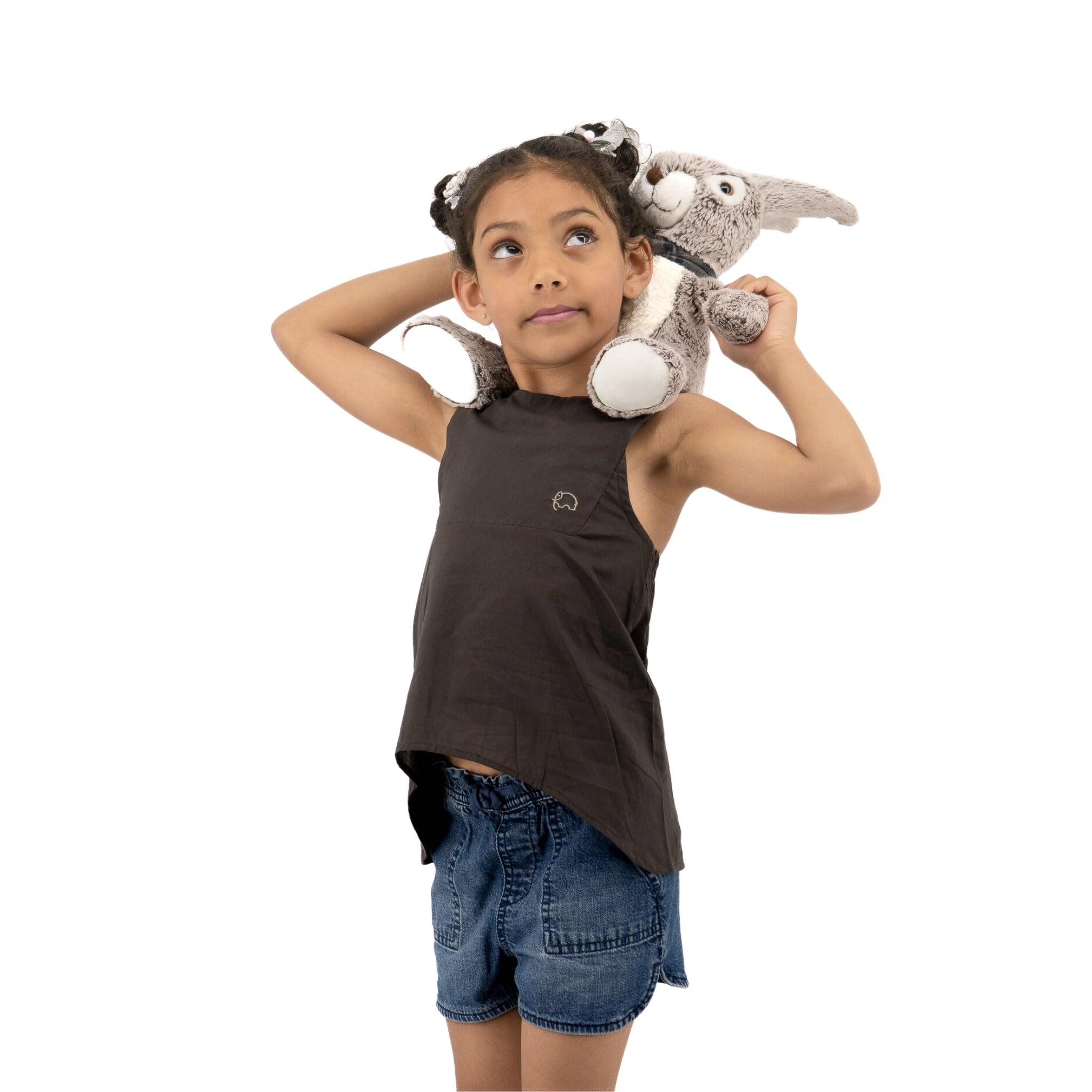 A young girl with a thoughtful expression, her hands on her head, wears a Karee Plum Kitten Cotton Bib Neck Top for Kids and holds a plush grey koala toy on her shoulder, against a white background.