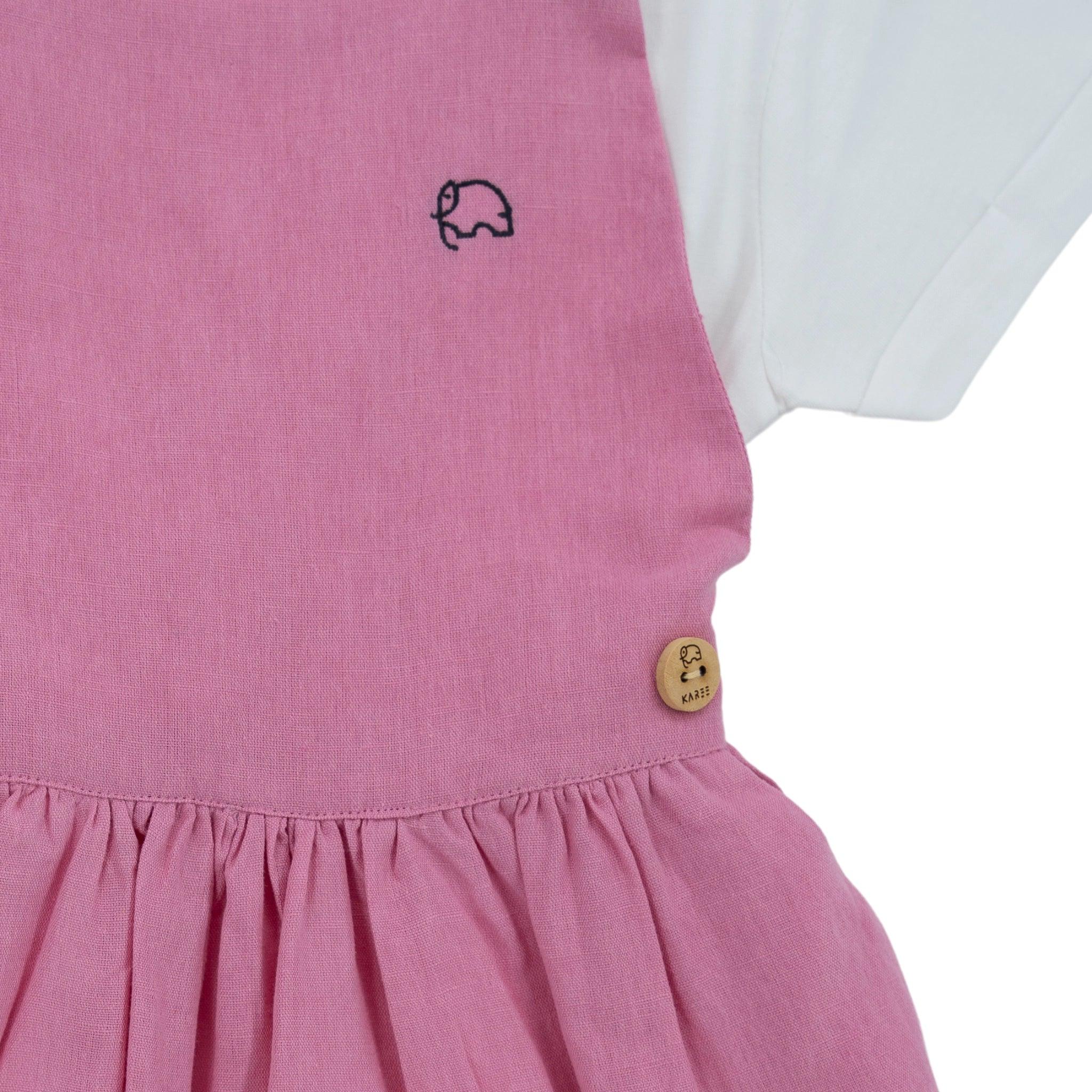 Close-up of a Karee Cashmere Rose Linen Pinafore, detailed with a small elephant embroidery and a wooden button engraved with a leaf design.