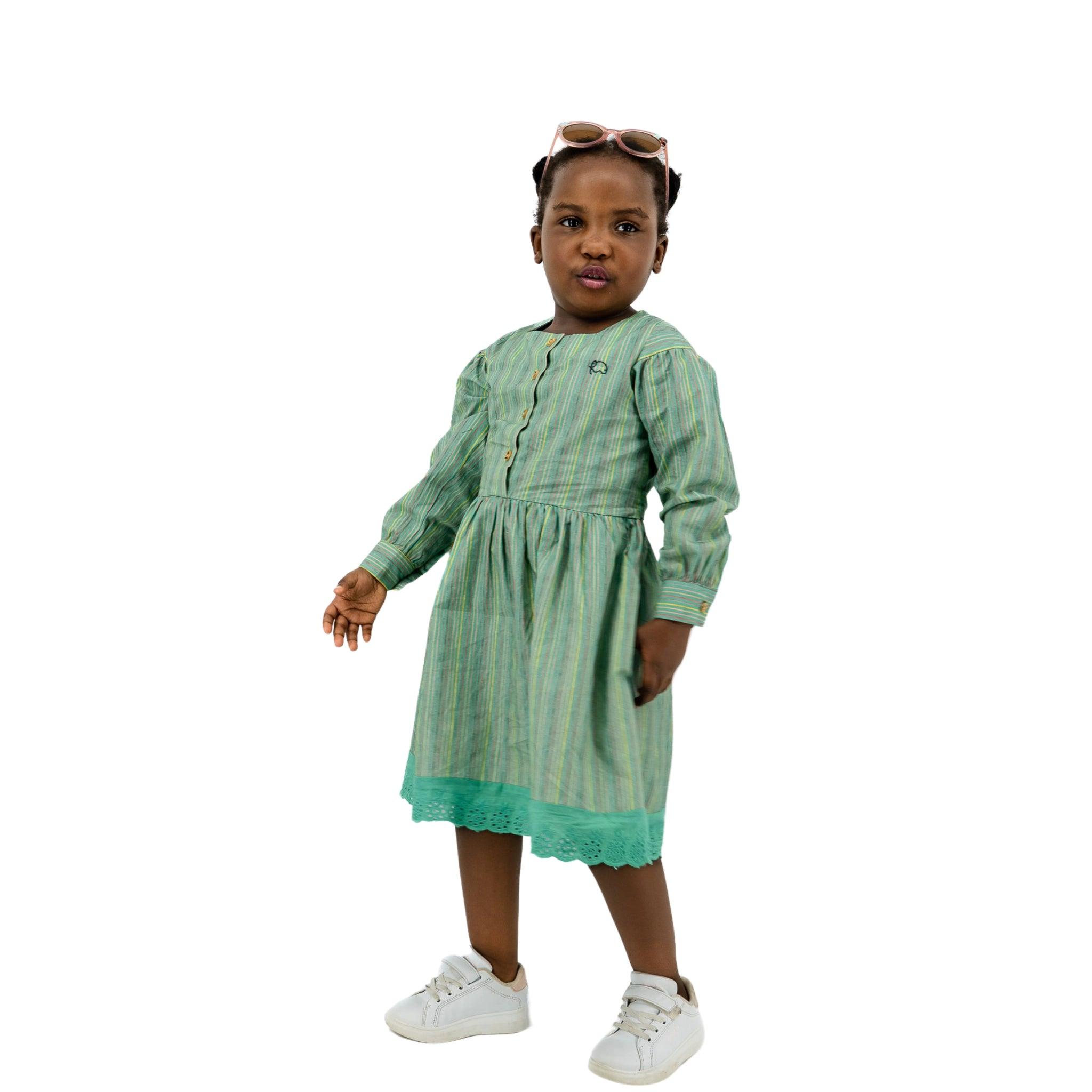 A young girl wearing a Karee Green Striped Long Puff Sleeve Cotton Dress and eco-friendly shoes.