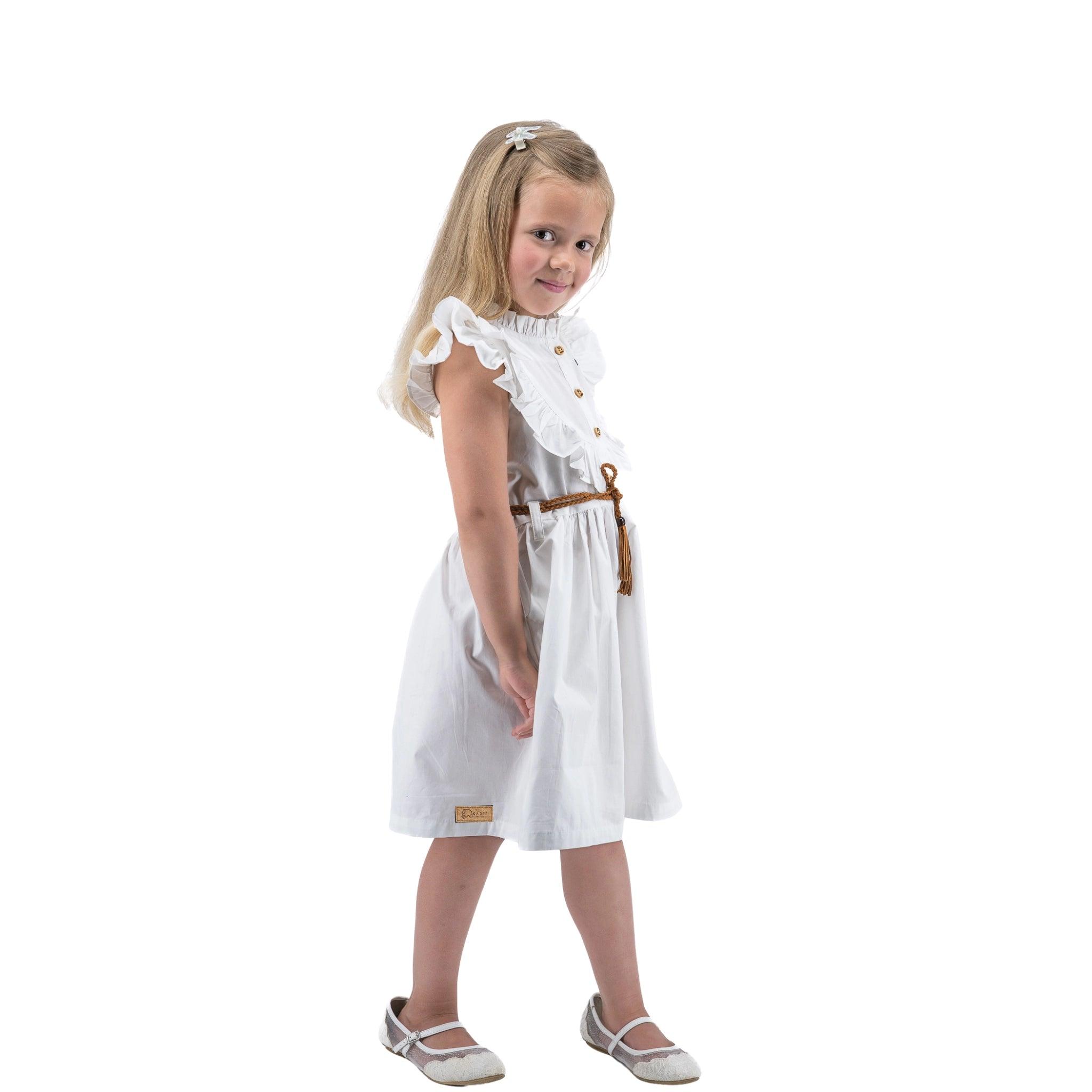 Young girl standing in a Karee Butterfly Sleeve Cotton Dress in White with a belt, looking over her shoulder with a slight smile, against a white background.