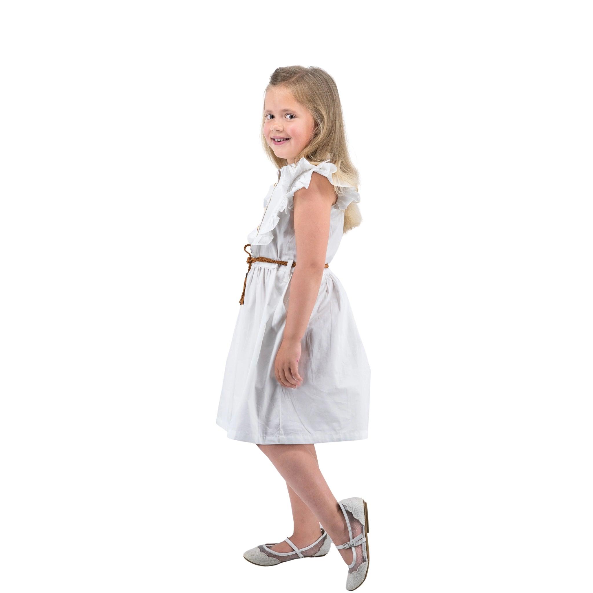 Young girl smiling, walking to her left side, dressed in a Karee white Butterfly Sleeve Cotton Dress with silver shoes, isolated on a white background.