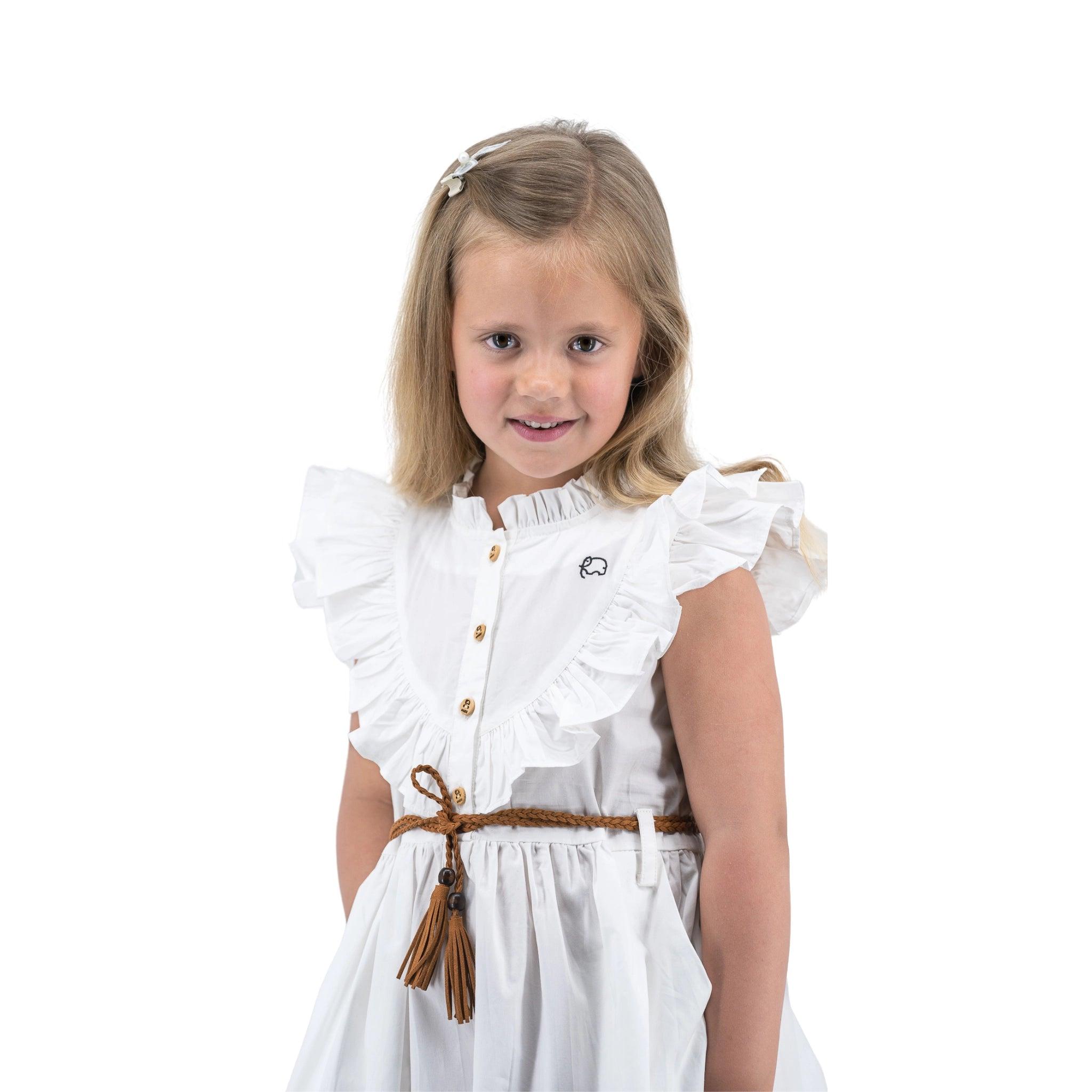 Young girl with blond hair wearing a Karee white butterfly sleeve cotton dress and a small bow clip, smiling slightly, standing against a white background.
