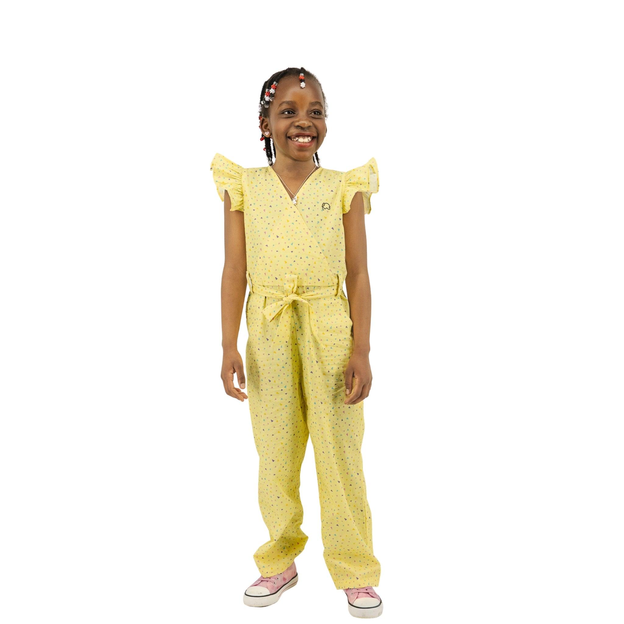 Young girl in a Karee Lemon Meringue Cotton V-Neck Jumpsuit and pink shoes with braided hair smiling against a white background.