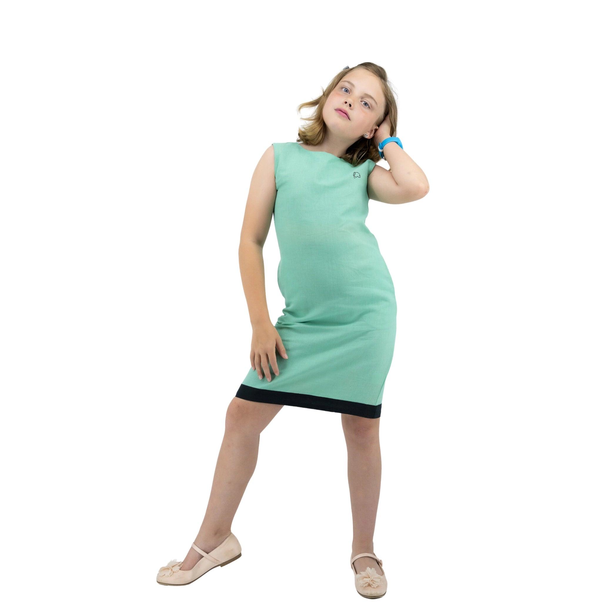 A young girl in a Karee Linen Cotton Round Neck Frock for Kids in Neptune Green posing with one hand on her hip and the other behind her head, standing against a white background.