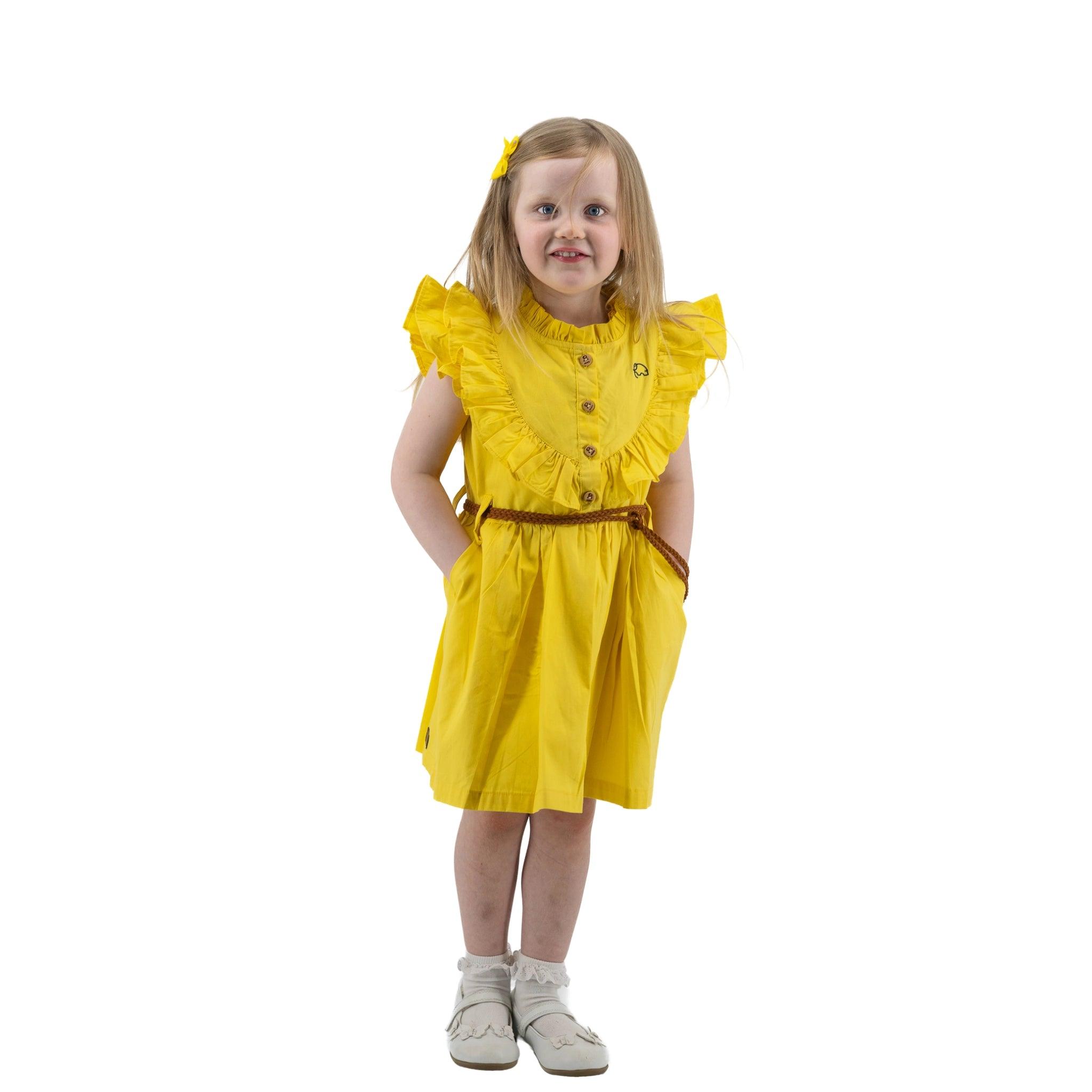 A young girl in a Karee yellow butterfly sleeve cotton dress and white sneakers stands with hands on hips, smiling at the camera on a white background.