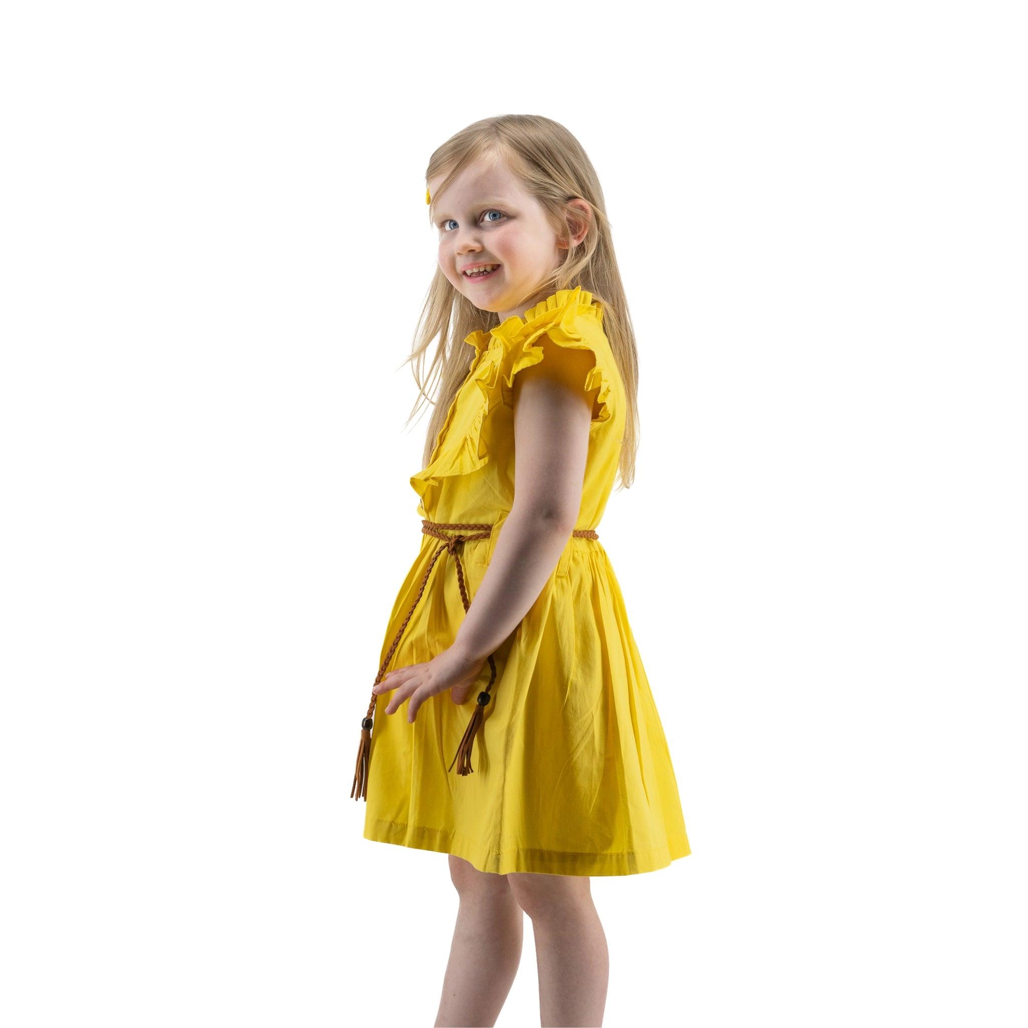 Young girl in a Karee yellow butterfly sleeve cotton dress with a brown belt, smiling over her shoulder, isolated on a white background.