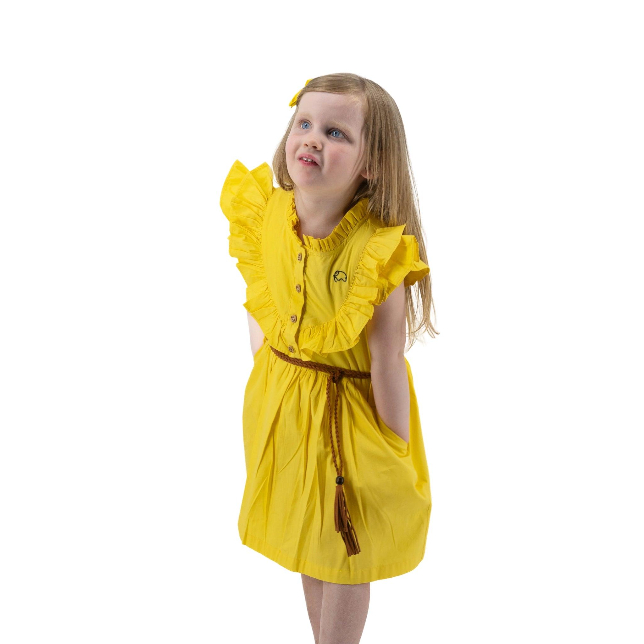 Young girl in a Karee yellow butterfly sleeve cotton dress looking up thoughtfully, standing isolated on a white background.
