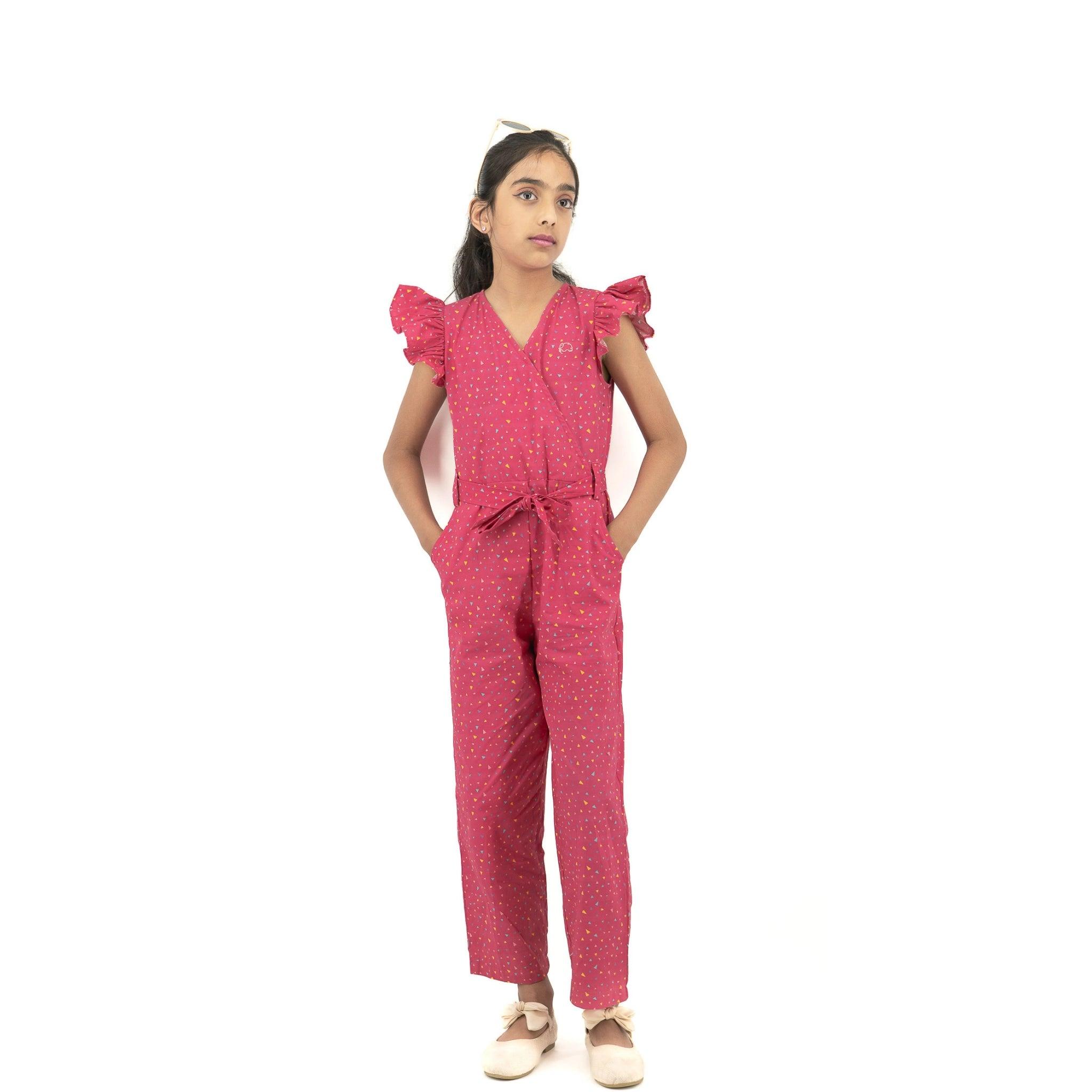 Young girl in a Red Rose cotton jumpsuit for girls by Karee, with ruffled sleeves, standing with hands on hips and looking to the side, against a white background.