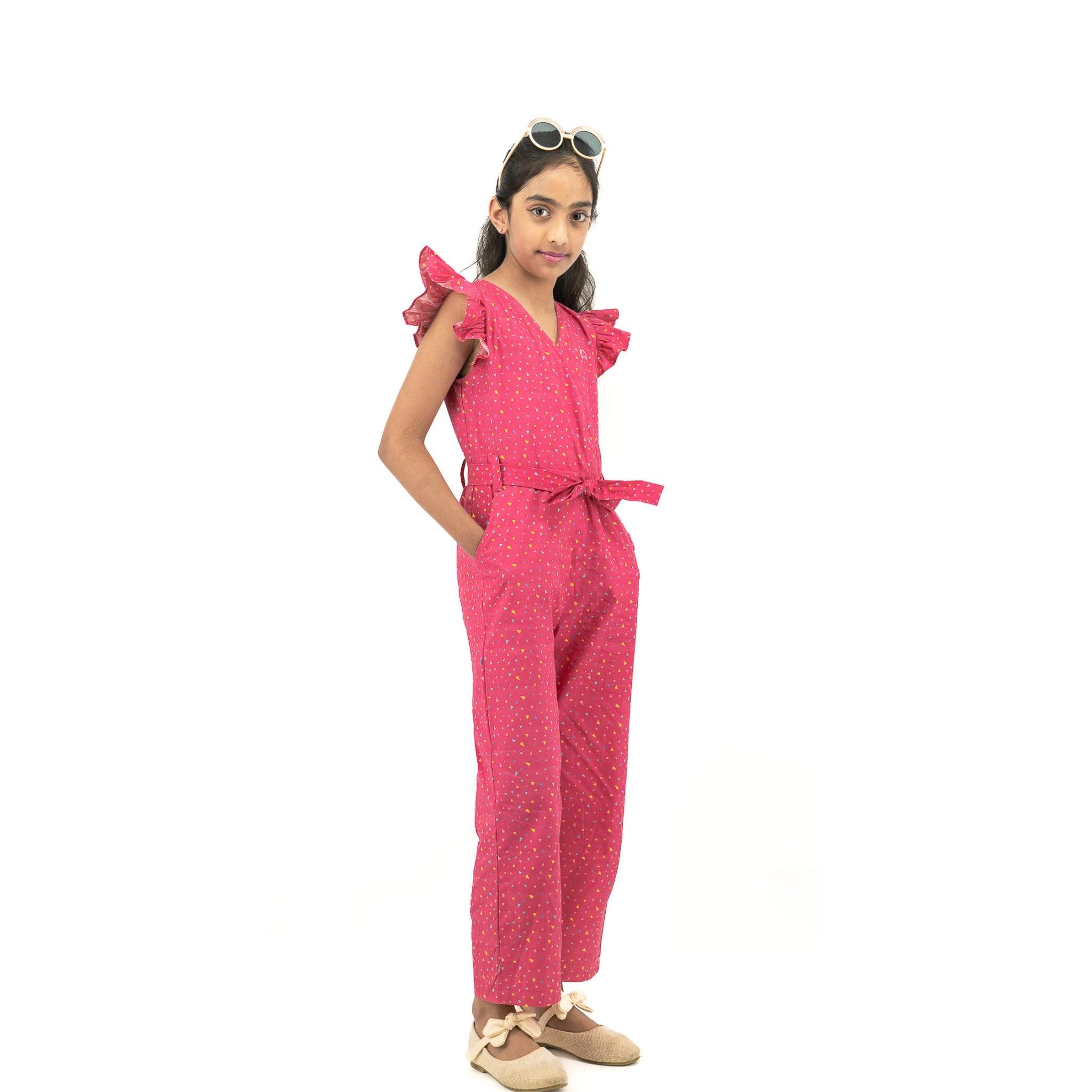 Young girl posing confidently in a Red Rose cotton jumpsuit for girls with a belt, hands on hips, wearing white sunglasses on her head, against a white background.