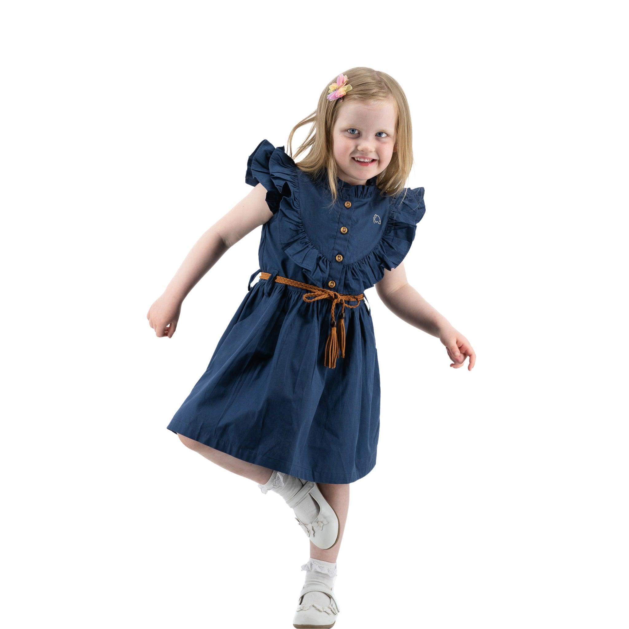 Young girl in a Karee navy blue butterfly sleeve cotton dress and white shoes twirling, with a joyful expression, isolated on white background.