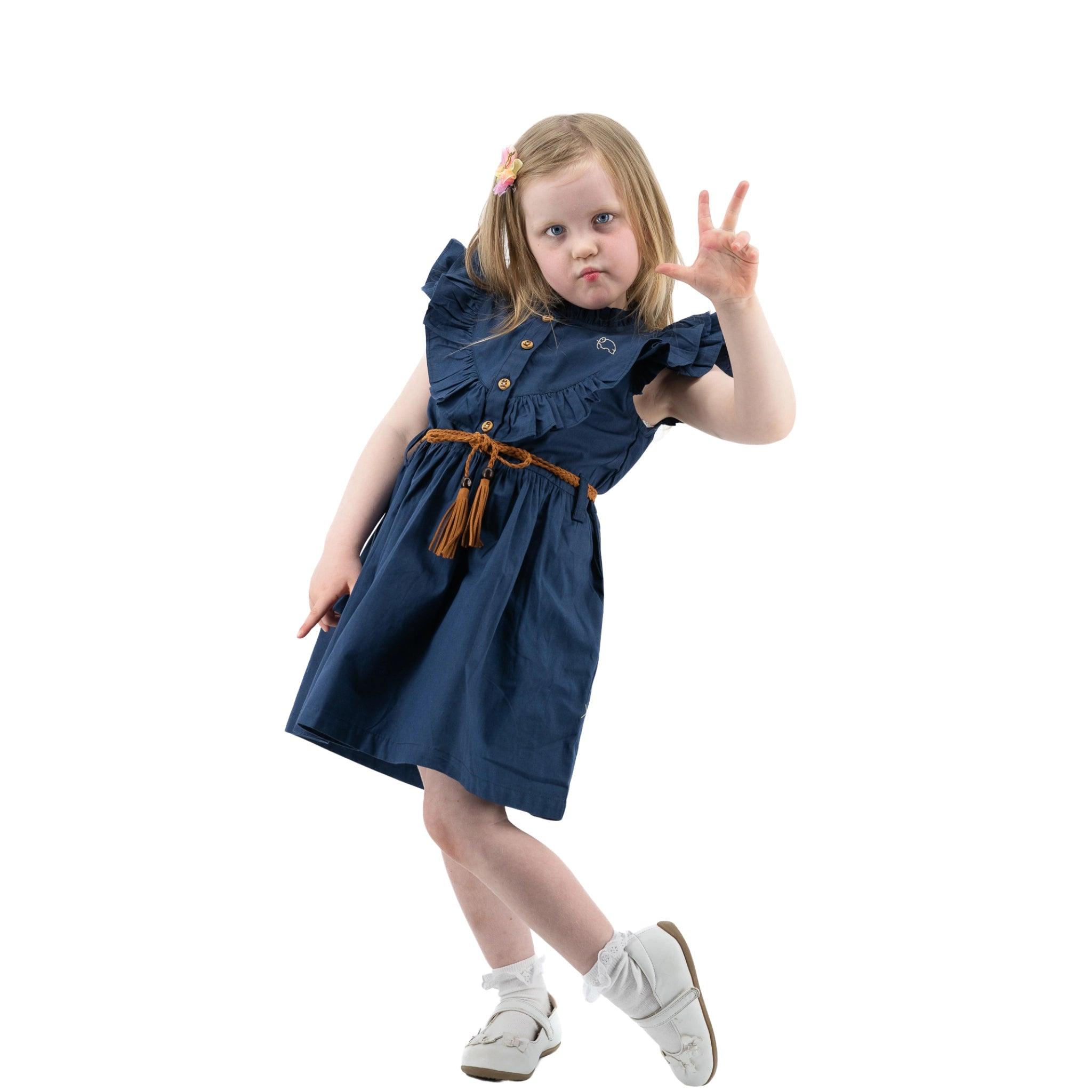 Young girl in Karee navy blue butterfly sleeve cotton dress making a peace sign with her hand, posing on one leg against a white background.