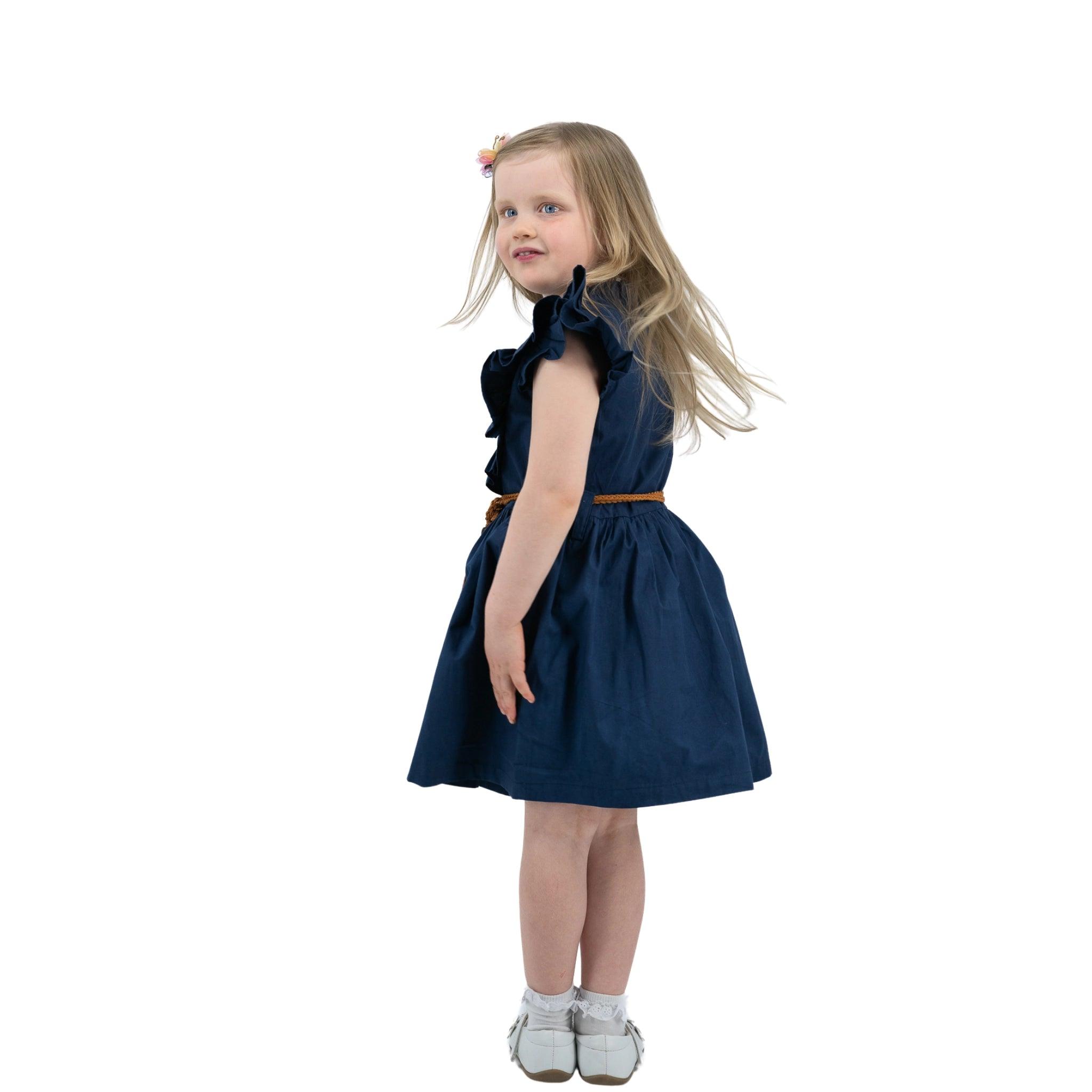 Young girl in a Karee Navy Blue Butterfly Sleeve Cotton Dress and white shoes standing isolated on a white background.