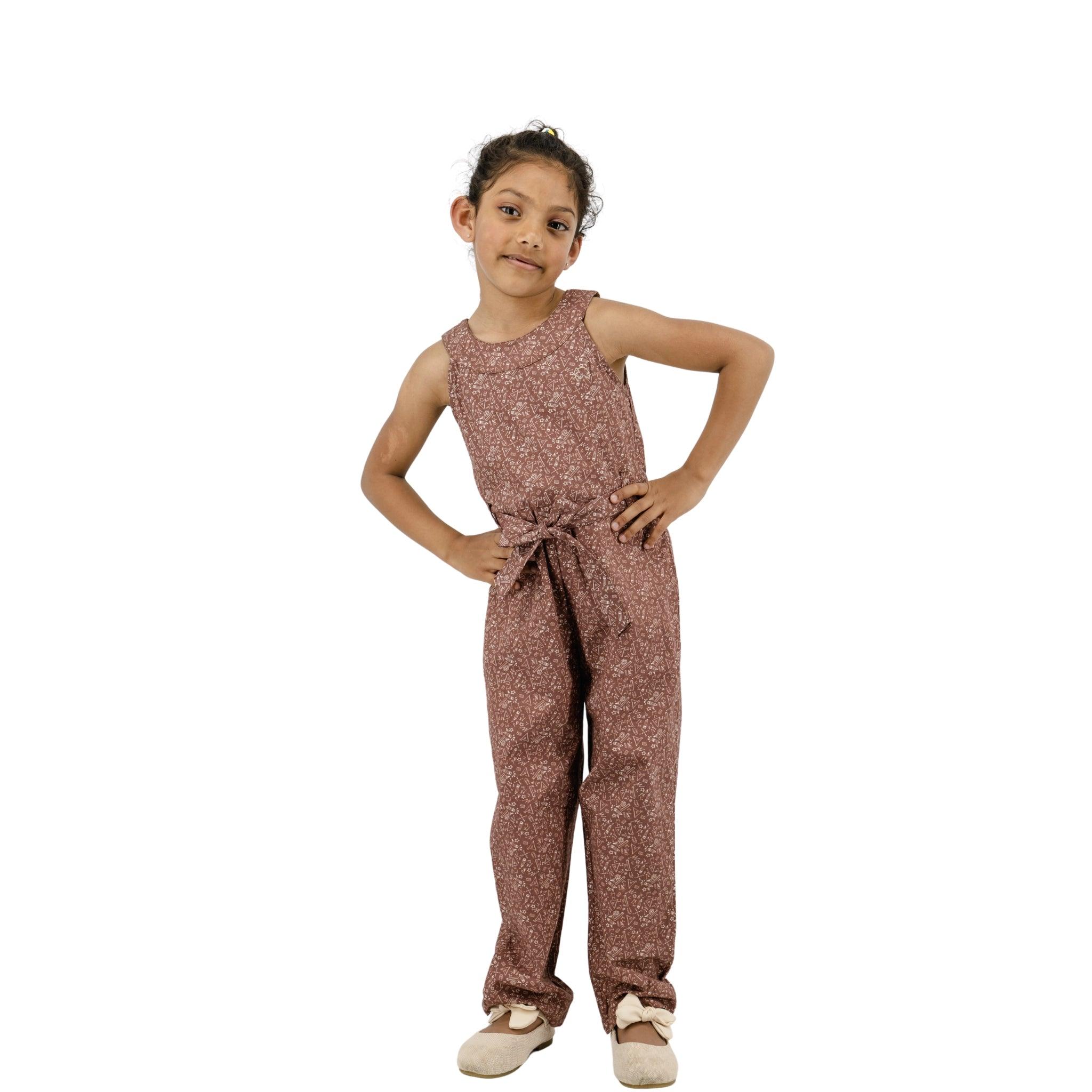 Young girl in a Karee Cocoa Brown Cotton Jumpsuit for Girls with a pattern, hands on her hips, posing confidently, isolated on a white background.