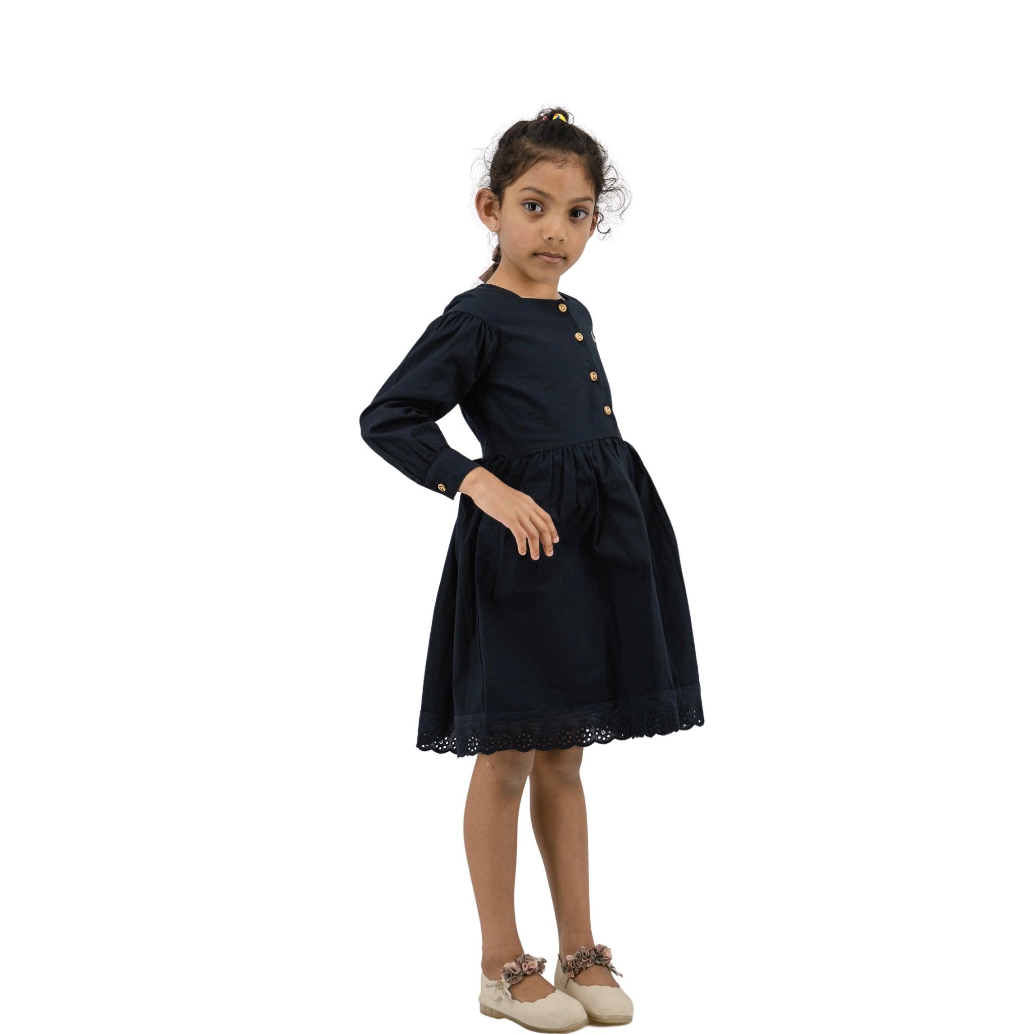 Young girl wearing a black Karee dress with long puff sleeves, button details, and lace trimming, standing sideways and looking towards the camera.
