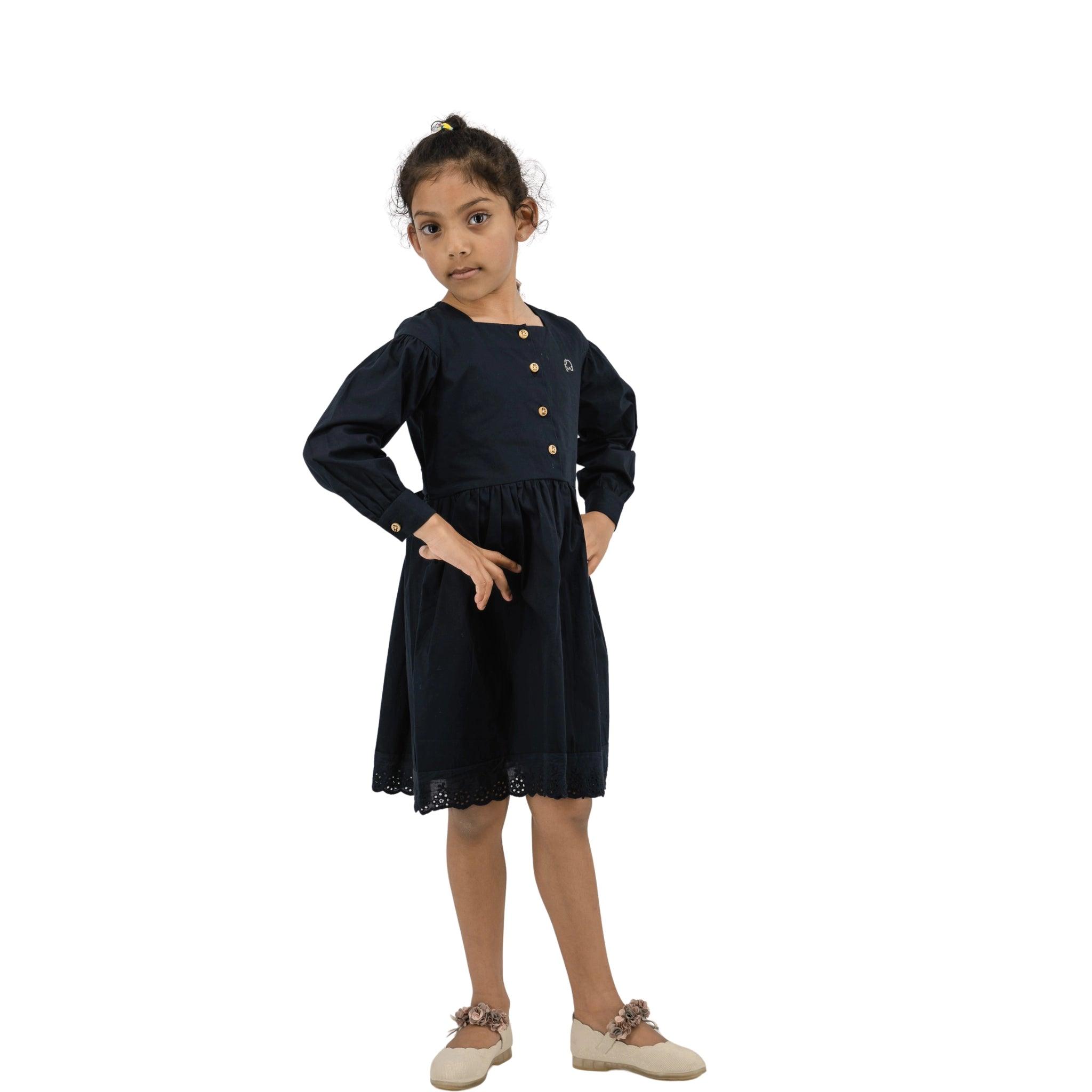 Young girl in a navy blue dress with long puff sleeves and beige shoes standing confidently with hands on hips against a white background.