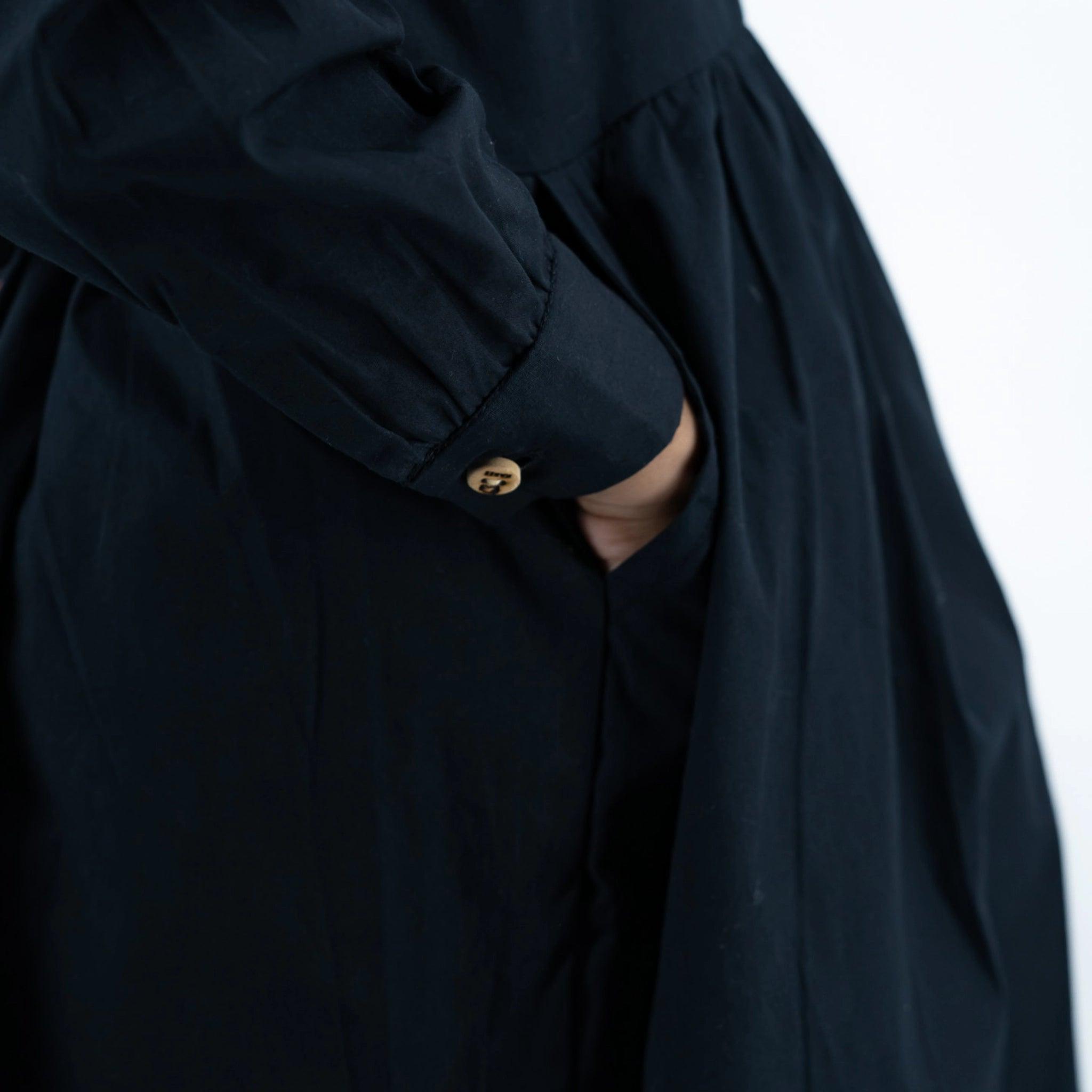 Close-up of a person wearing a dark navy trench coat with long puff sleeves, focusing on the cuff and golden button by Karee.