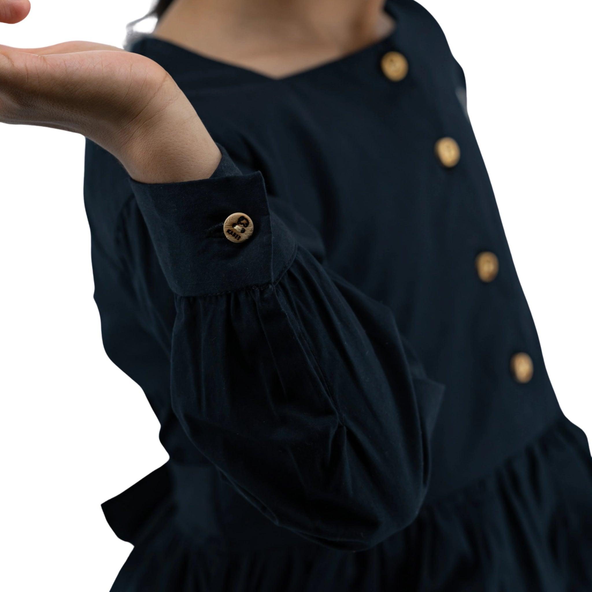 Close-up of a woman dressed in a Karee navy blue dress with long puff sleeves and gold buttons, extending her hand, isolated on a white background.