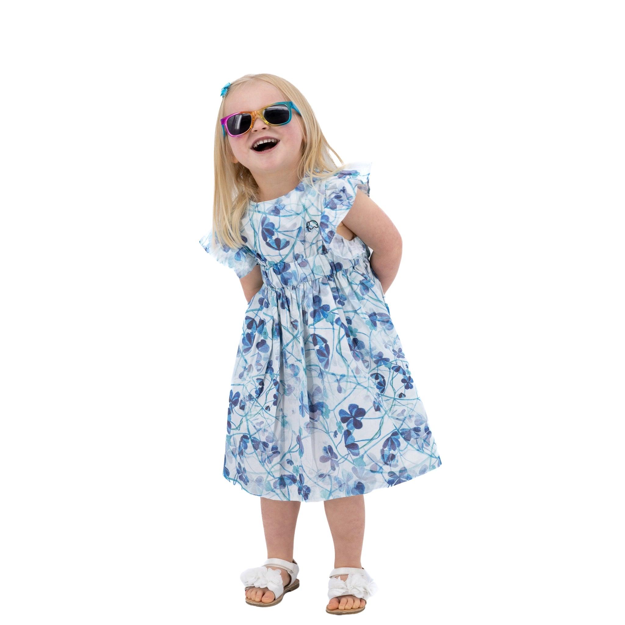 A young girl in a Karee Blue Cotton Floral Dress for Girls and sunglasses laughing joyfully, isolated on a white background.