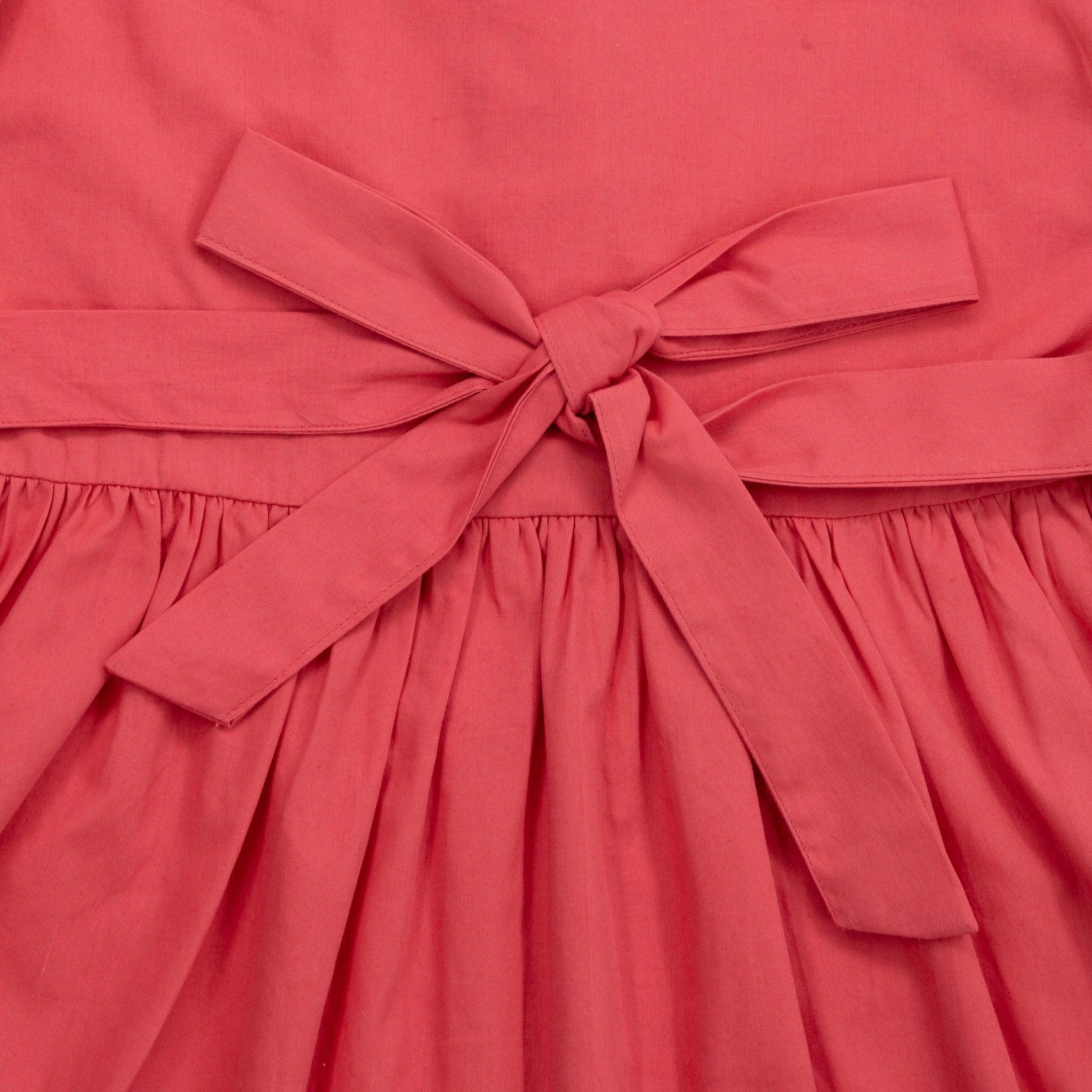 Close-up of a coral pink fabric with a decorative bow and gathered pleats on a Karee red long puff sleeve cotton dress.