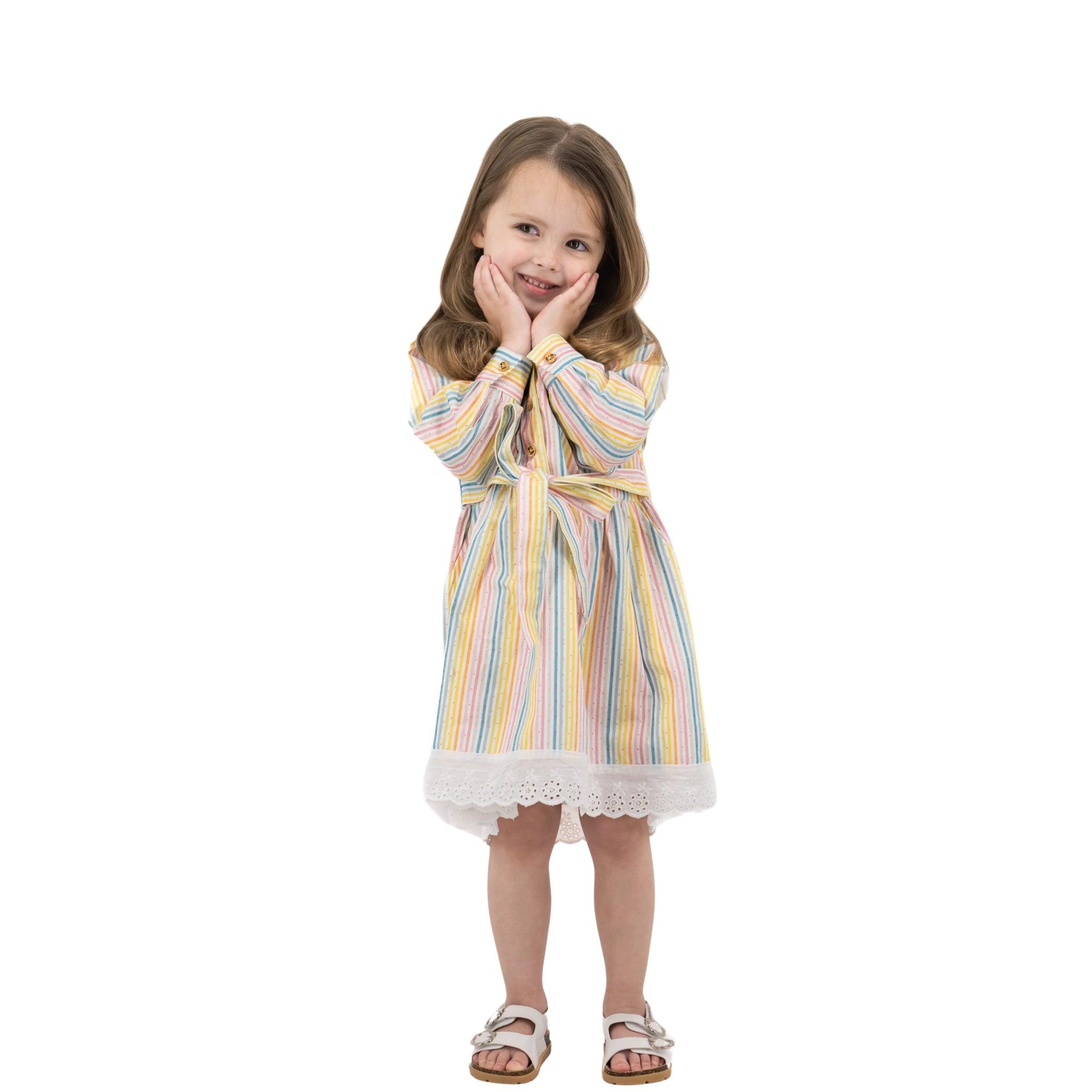 Young girl in a Karee Long Puff Sleeve White Cotton Dress with Stripes, standing and smiling with hands on cheeks, isolated on a white background.