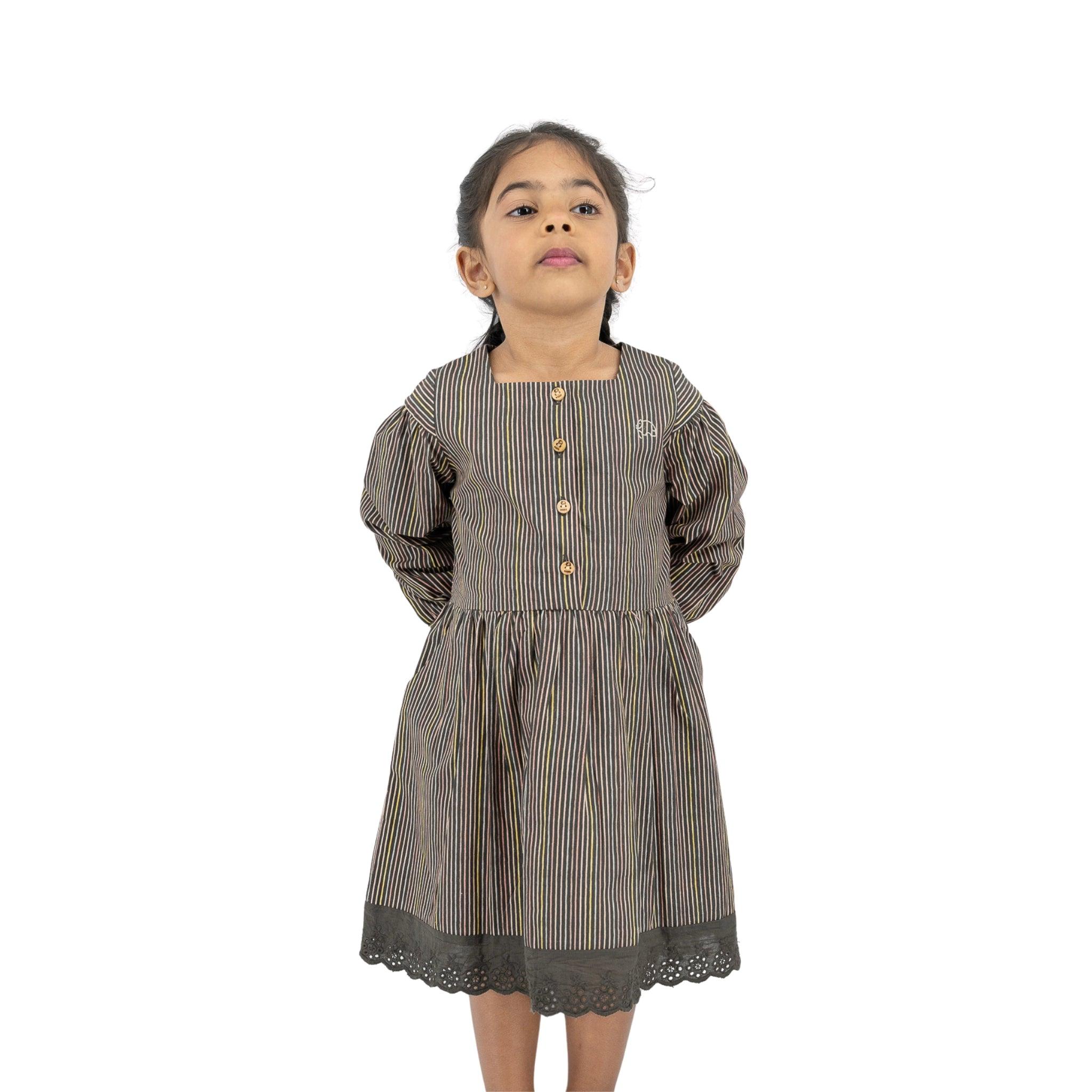 A young girl in a Karee black striped full sleeve cotton dress with lace hem stands confidently, looking upward, isolated on a white background.