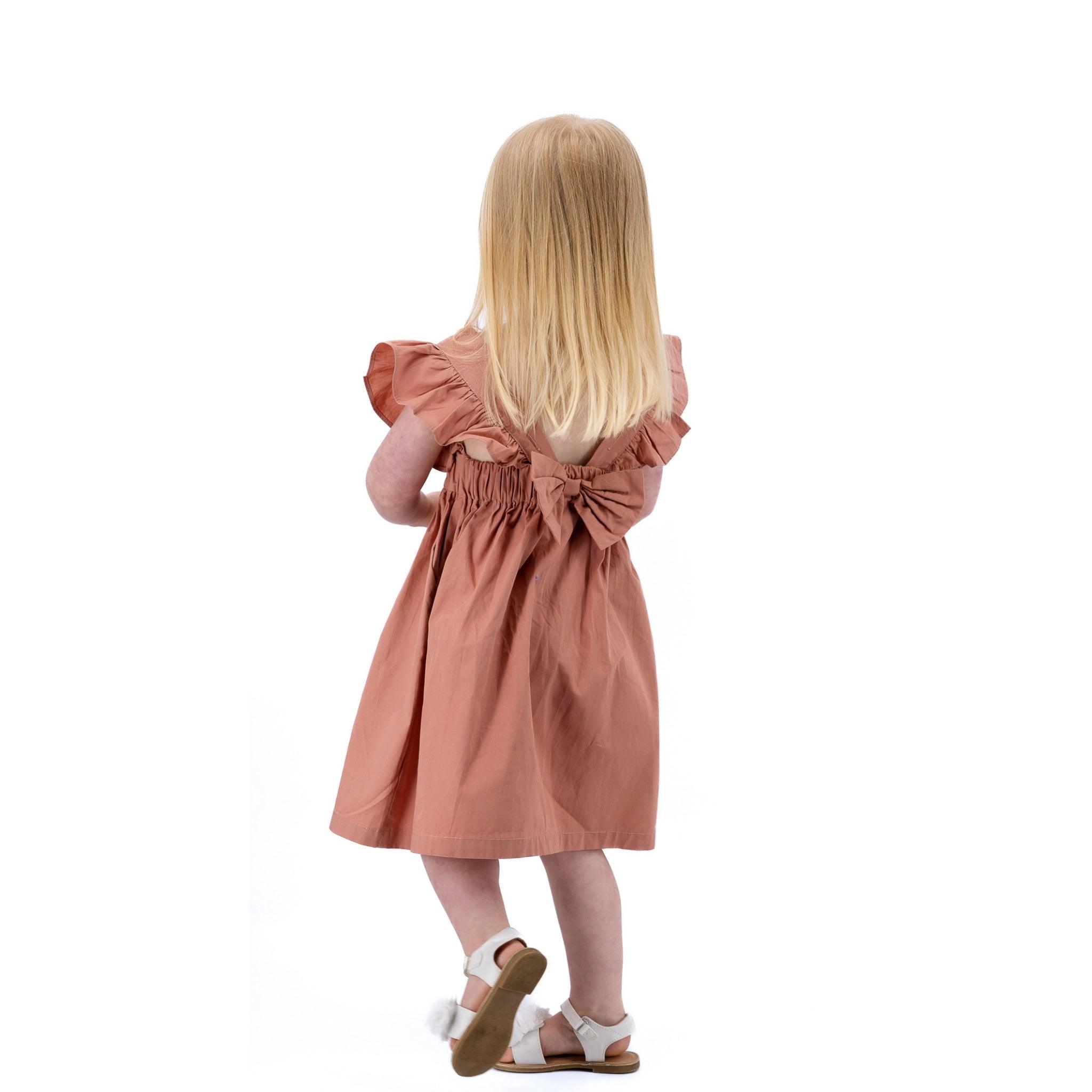 Young girl in a Brick Dust Cotton Floral Dress for Girls by Karee seen from behind, standing against a white background.