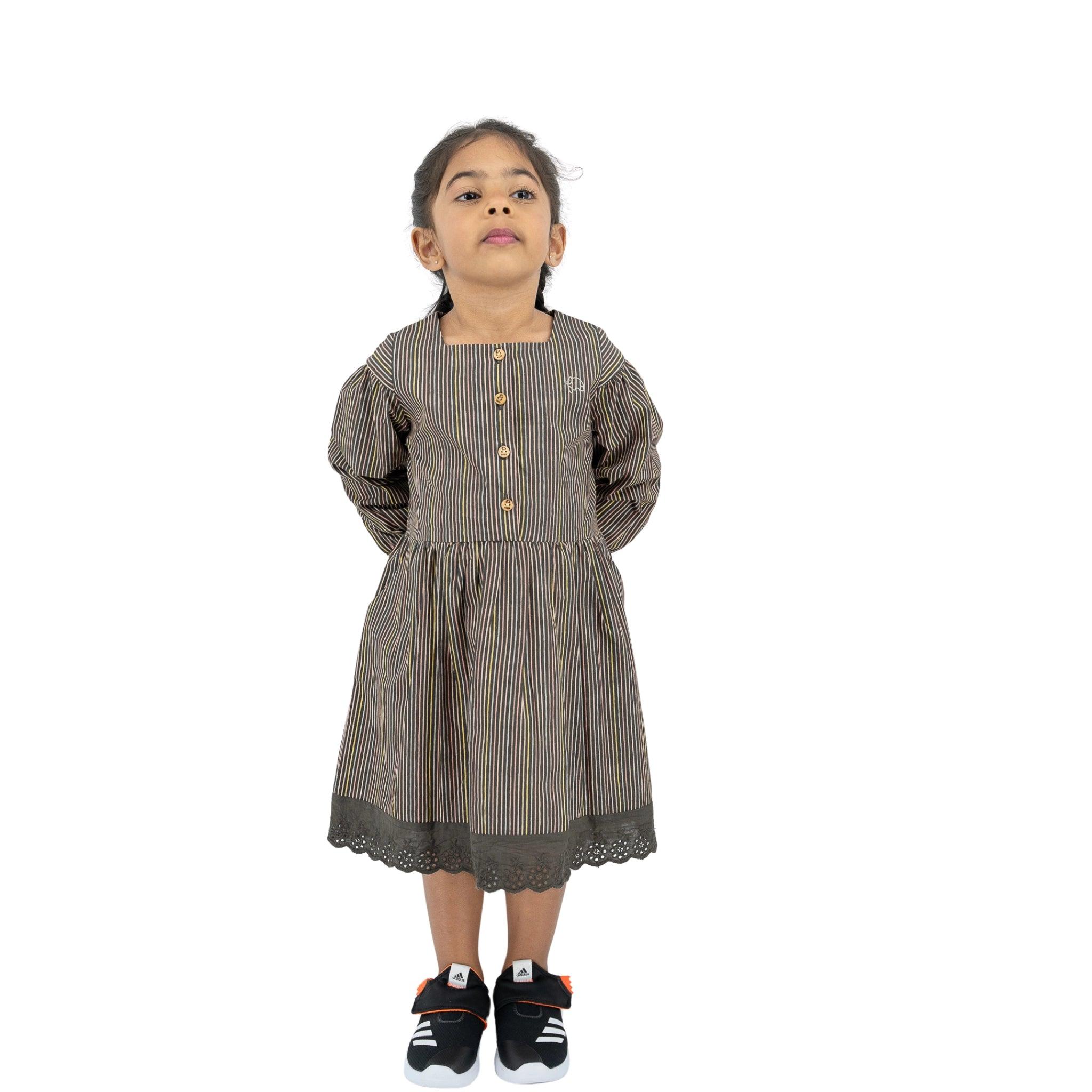 Young girl standing, looking upwards, wearing a Karee black striped full sleeve cotton dress and sneakers, isolated on a white background.