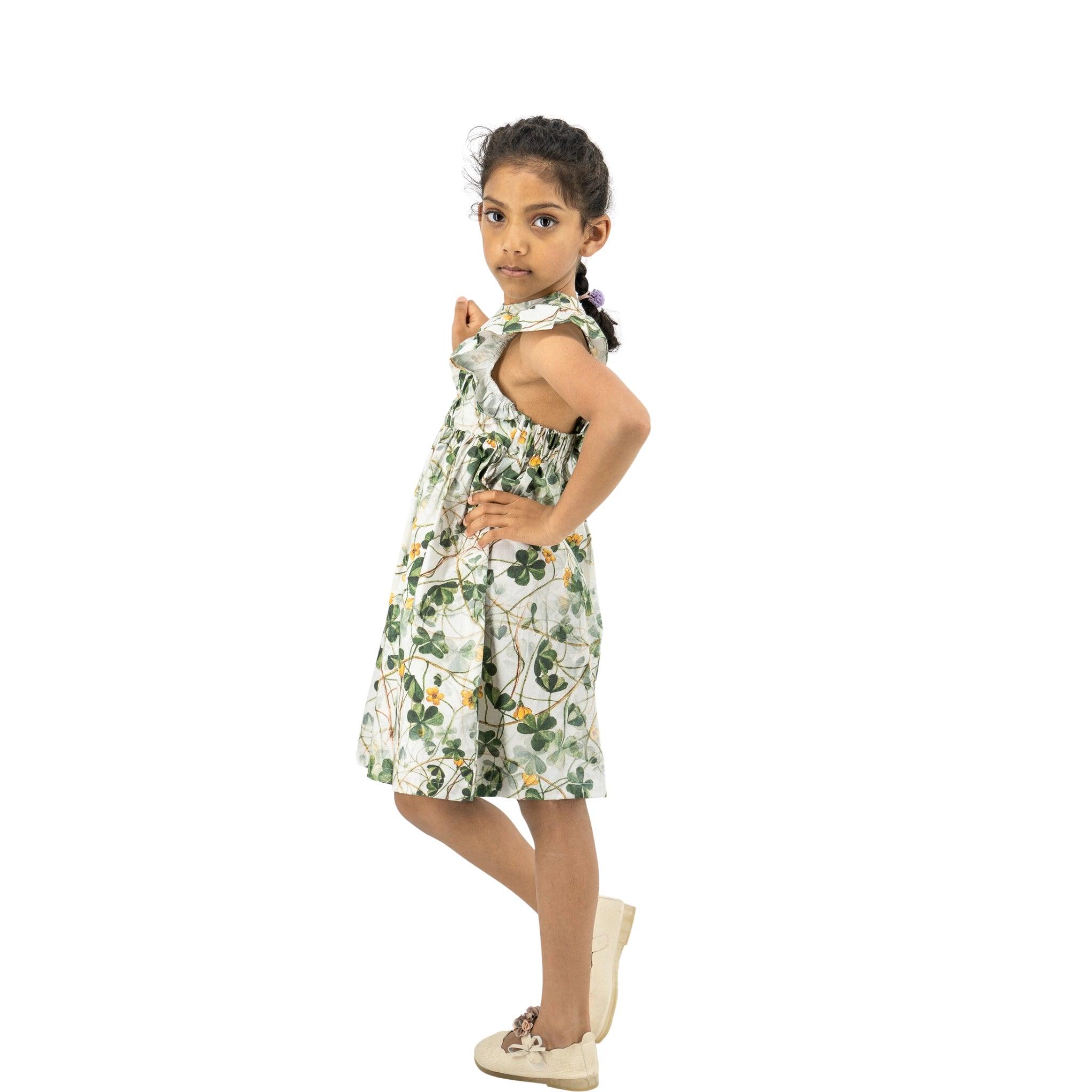 Young girl posing in a Karee green floral cotton dress for girls and white shoes, standing sideways with a confident gaze, isolated on a white background.