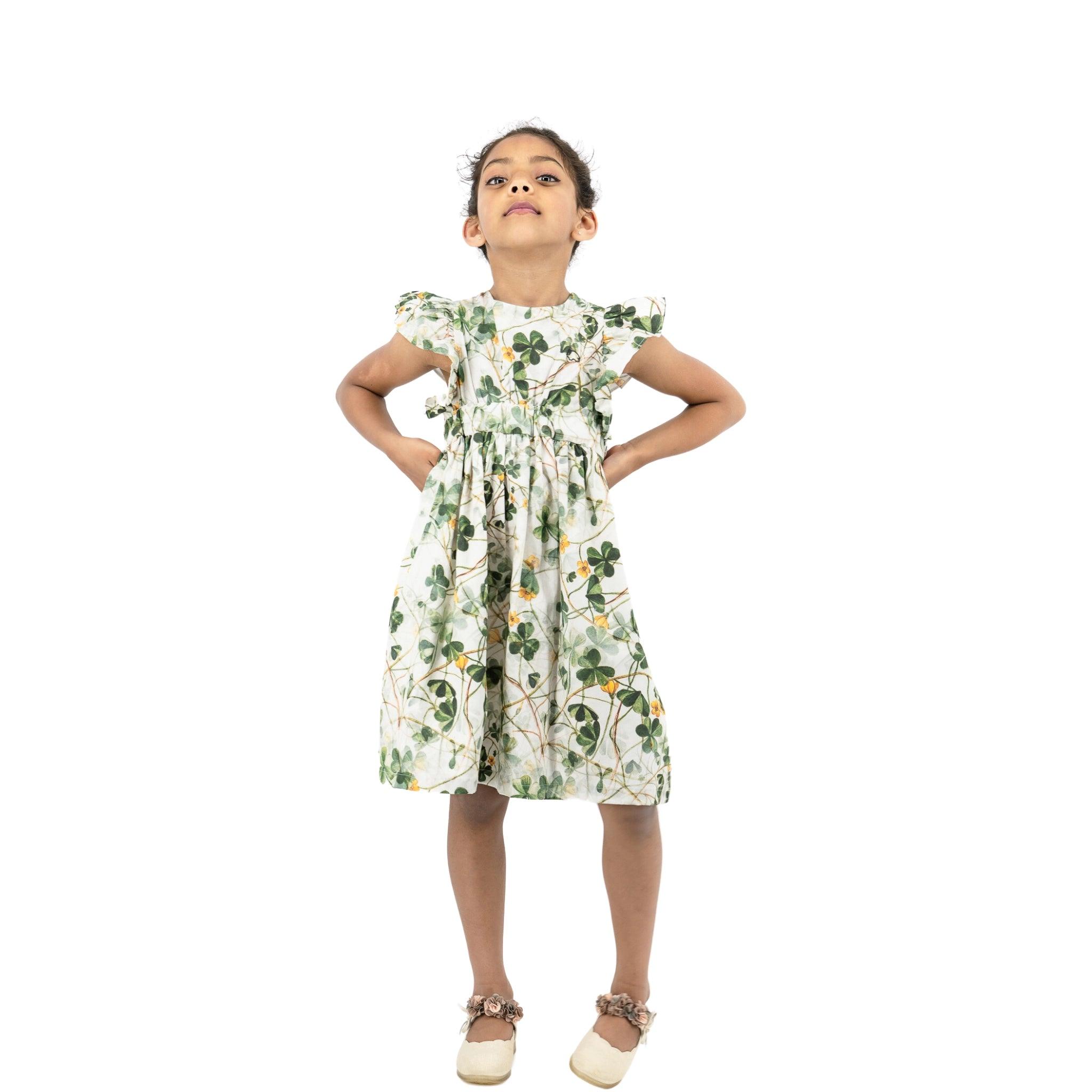 Young girl standing with hands on hips, wearing a Karee Green Floral Cotton Dress for Girls and looking confident, isolated on a white background.