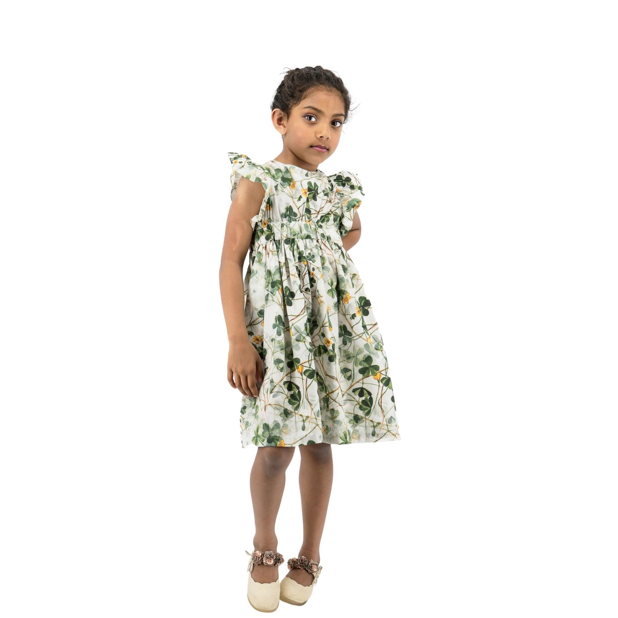 Young girl in a Karee green floral cotton dress standing isolated on a white background, looking to the side with a thoughtful expression.