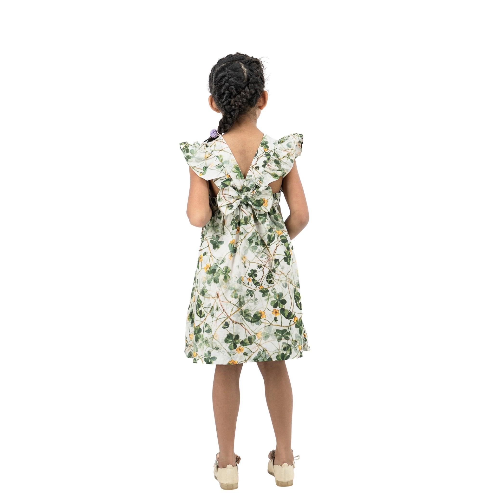 Young girl seen from behind, wearing a Karee green floral cotton dress with ruffled sleeves and braided hair, standing against a white background.