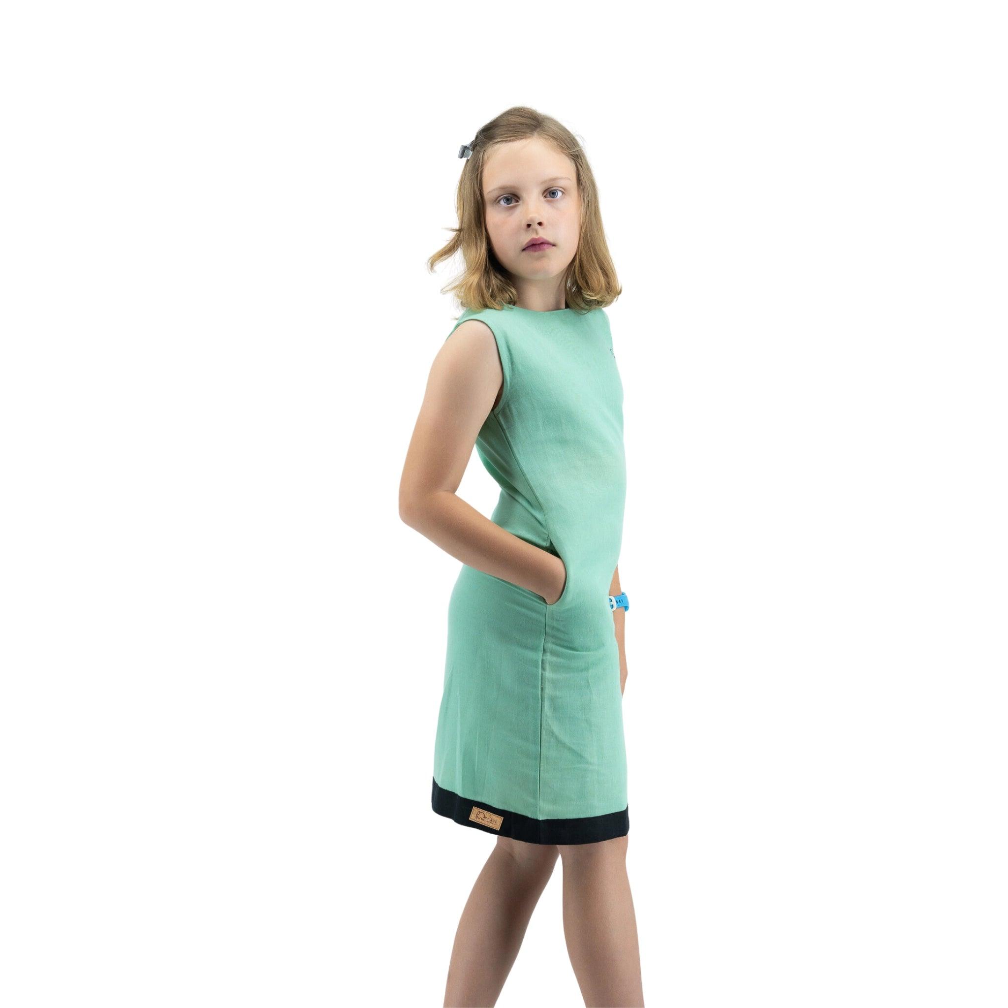 Young girl in a Karee Neptune Green Linen Cotton Round Neck Frock and sunglasses posing with hands on hips against a white background.