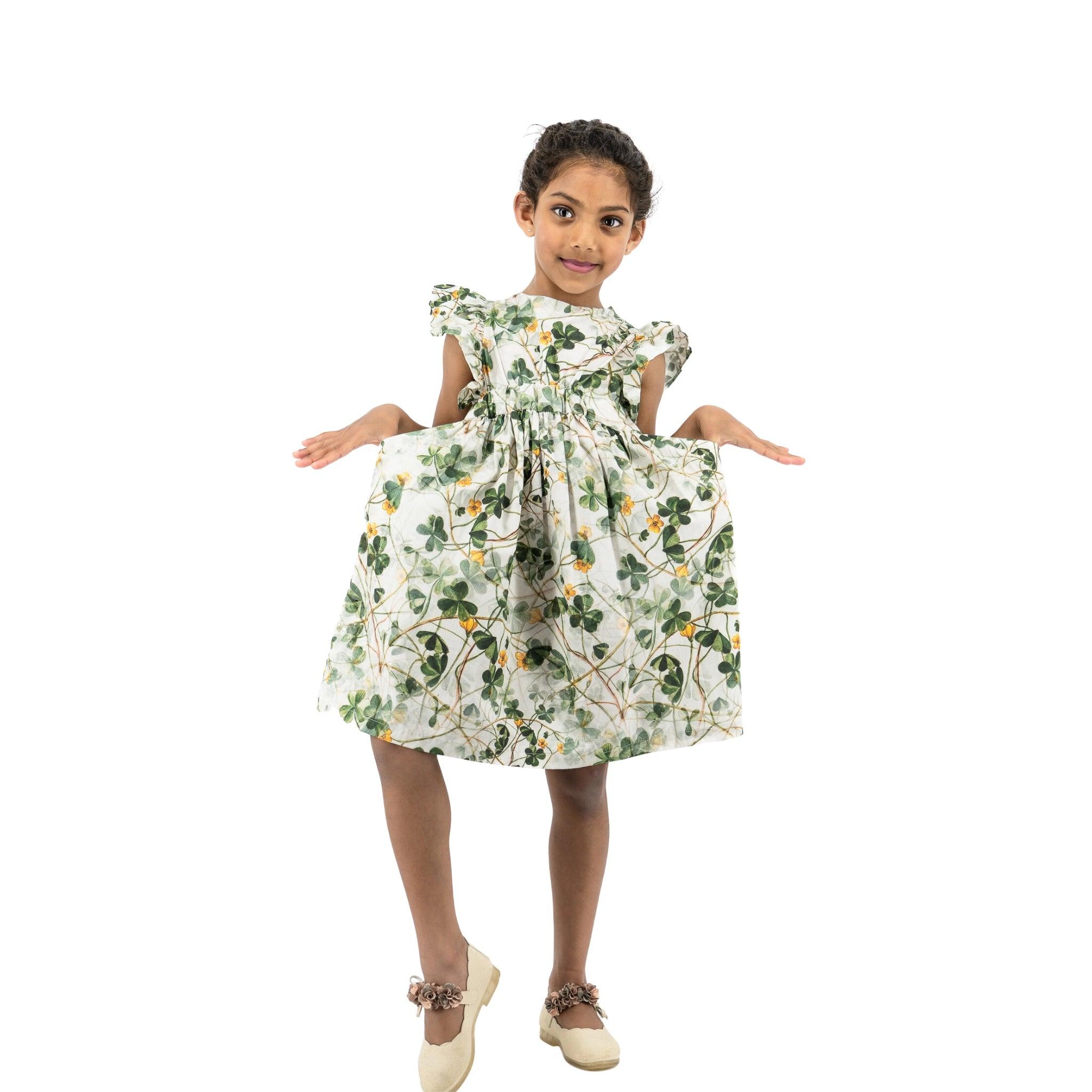 Young girl in a Karee green floral cotton dress for girls standing with arms slightly raised, smiling at the camera, isolated on a white background.