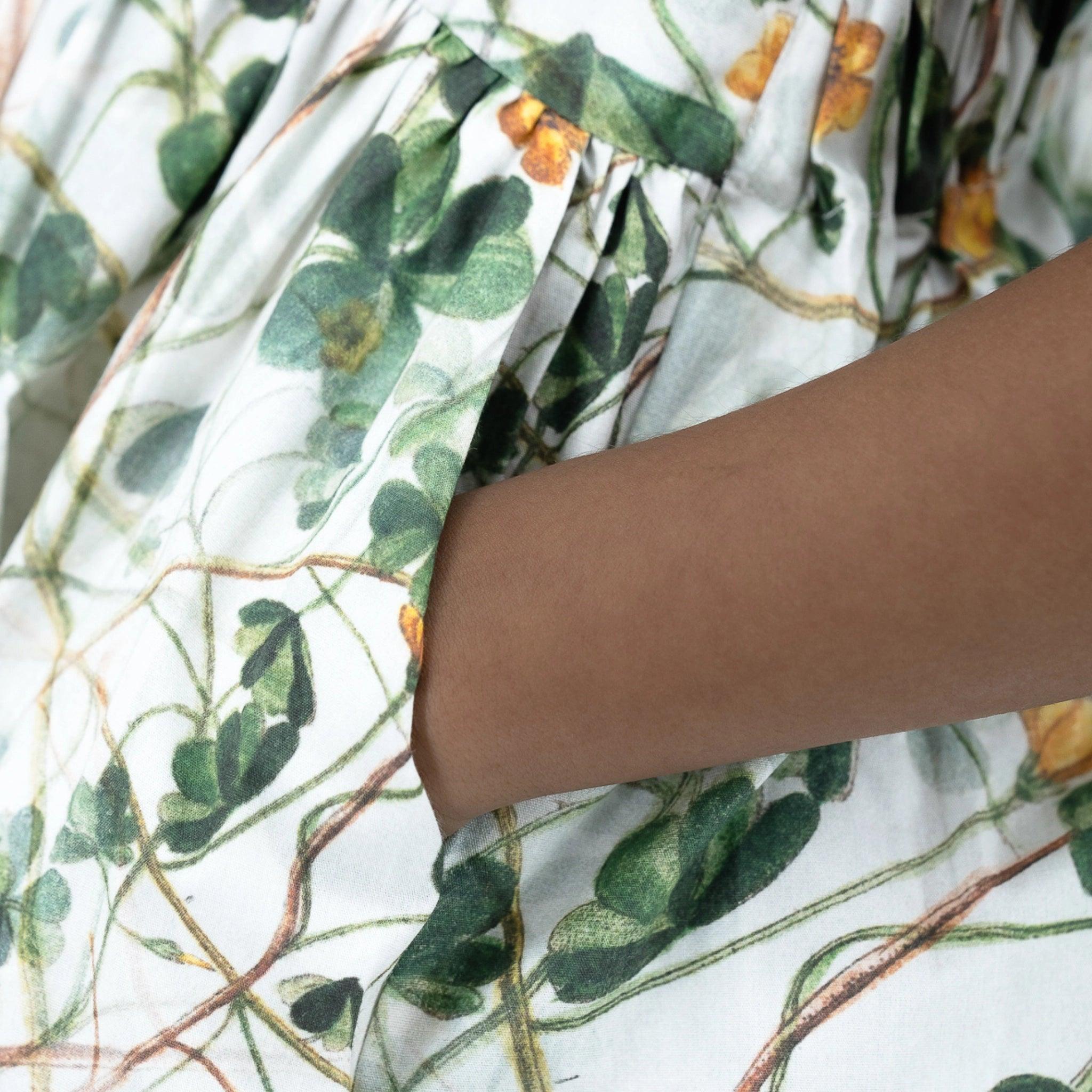 Close-up of a person's arm against a Karee green floral cotton dress for girls, focusing on the texture and colors of the material and skin.
