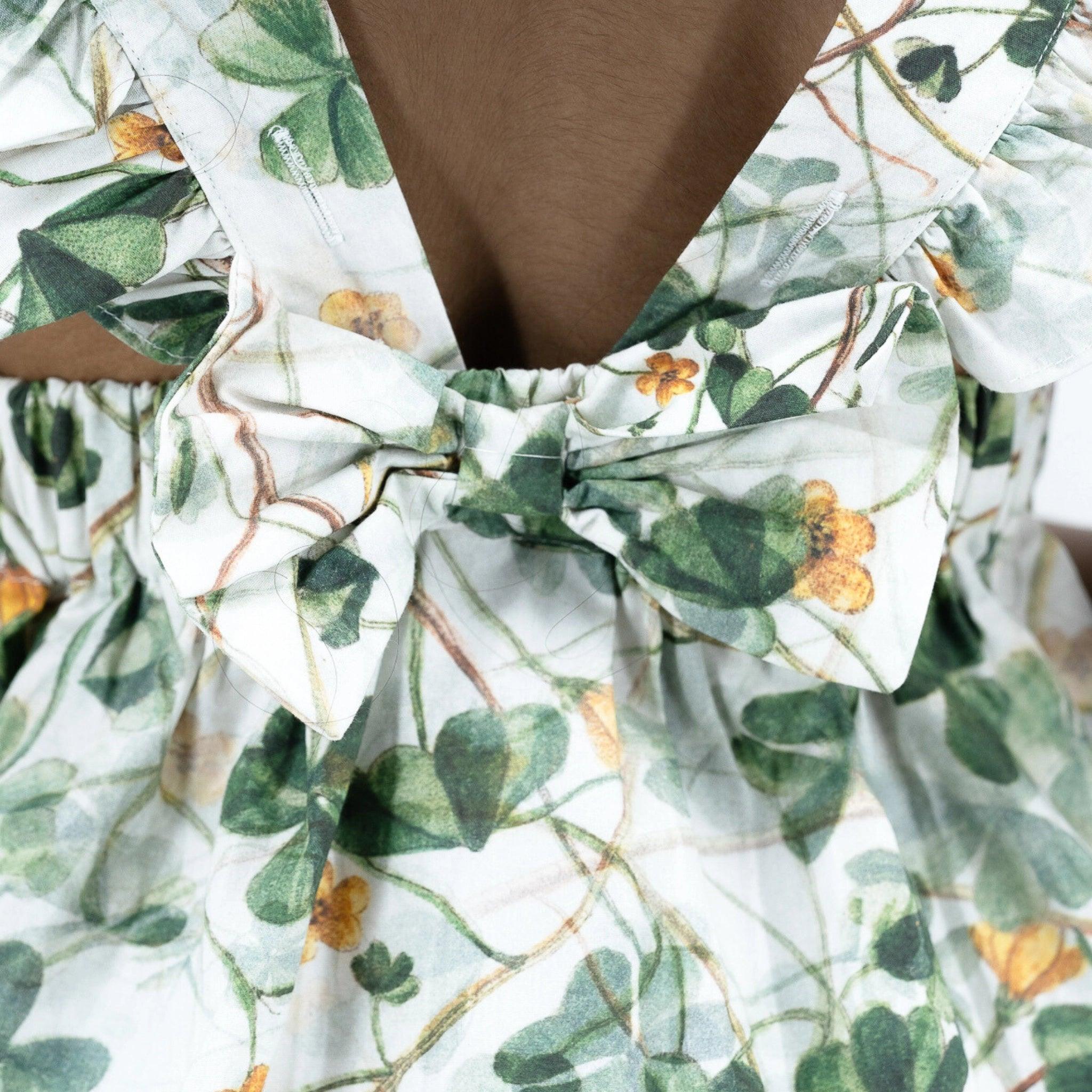Close-up of a person wearing a Karee sustainable green floral cotton dress for girls with a bow detail at the back.
