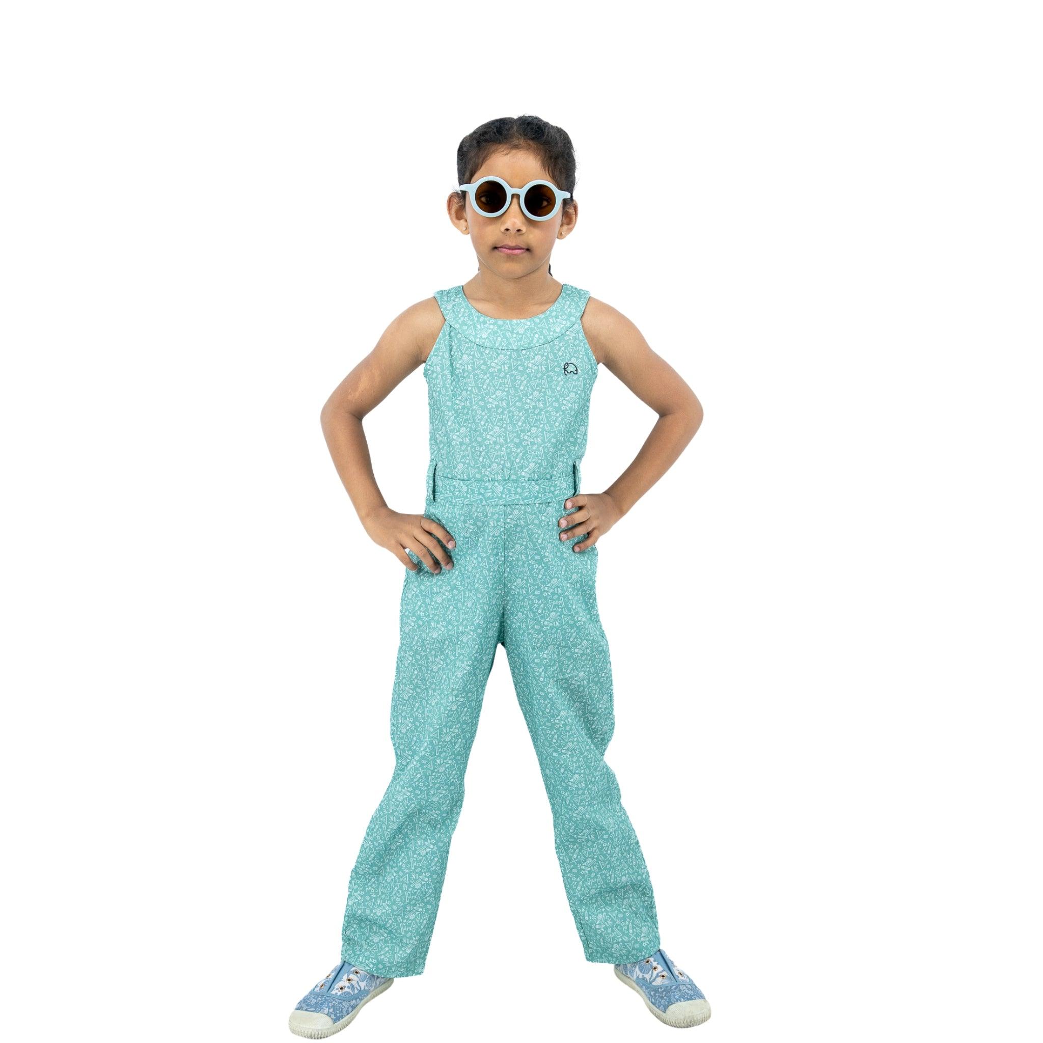 A young girl stands confidently wearing a Karee smoke green cotton jumpsuit and sunglasses, hands on hips, against a white background.