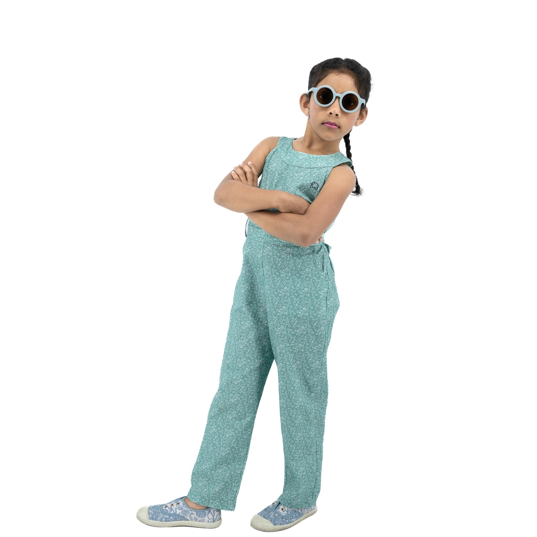 Young girl wearing sunglasses, with arms crossed, dressed in a sustainable fashion Karee Smoke Green Cotton Jumpsuit For Girls, standing against a plain white background.