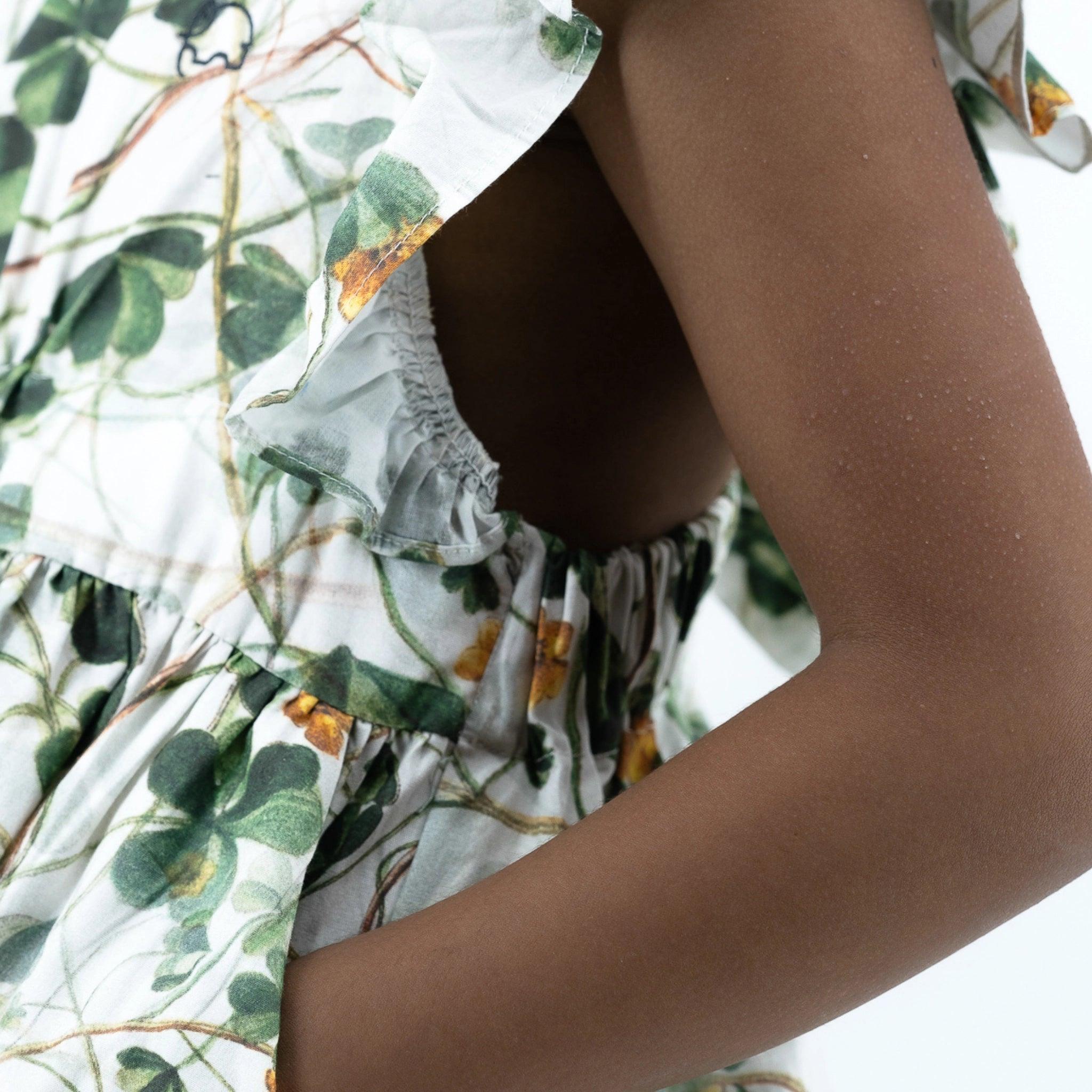 Close-up of a person's torso wearing a Karee green floral cotton dress for girls, focusing on the sustainable fashion fabric detail and arm.