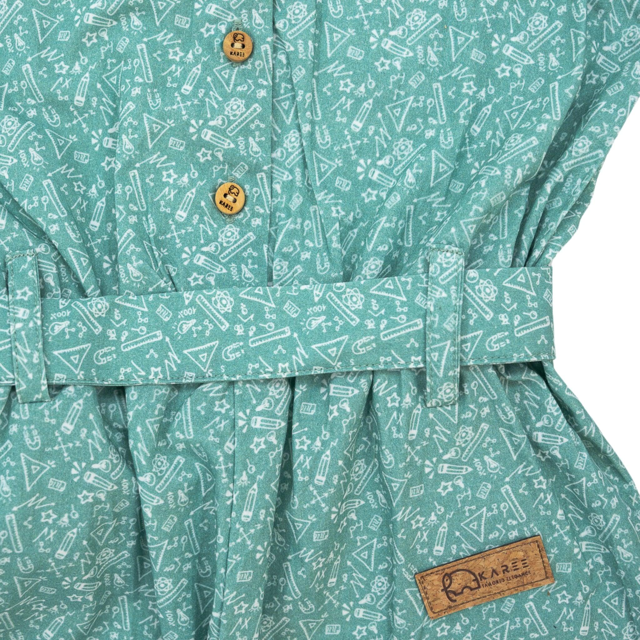 Close-up of a Karee smoke green cotton jumpsuit for girls with a white geometric pattern, featuring a button and a branded brown label on the waistband.
