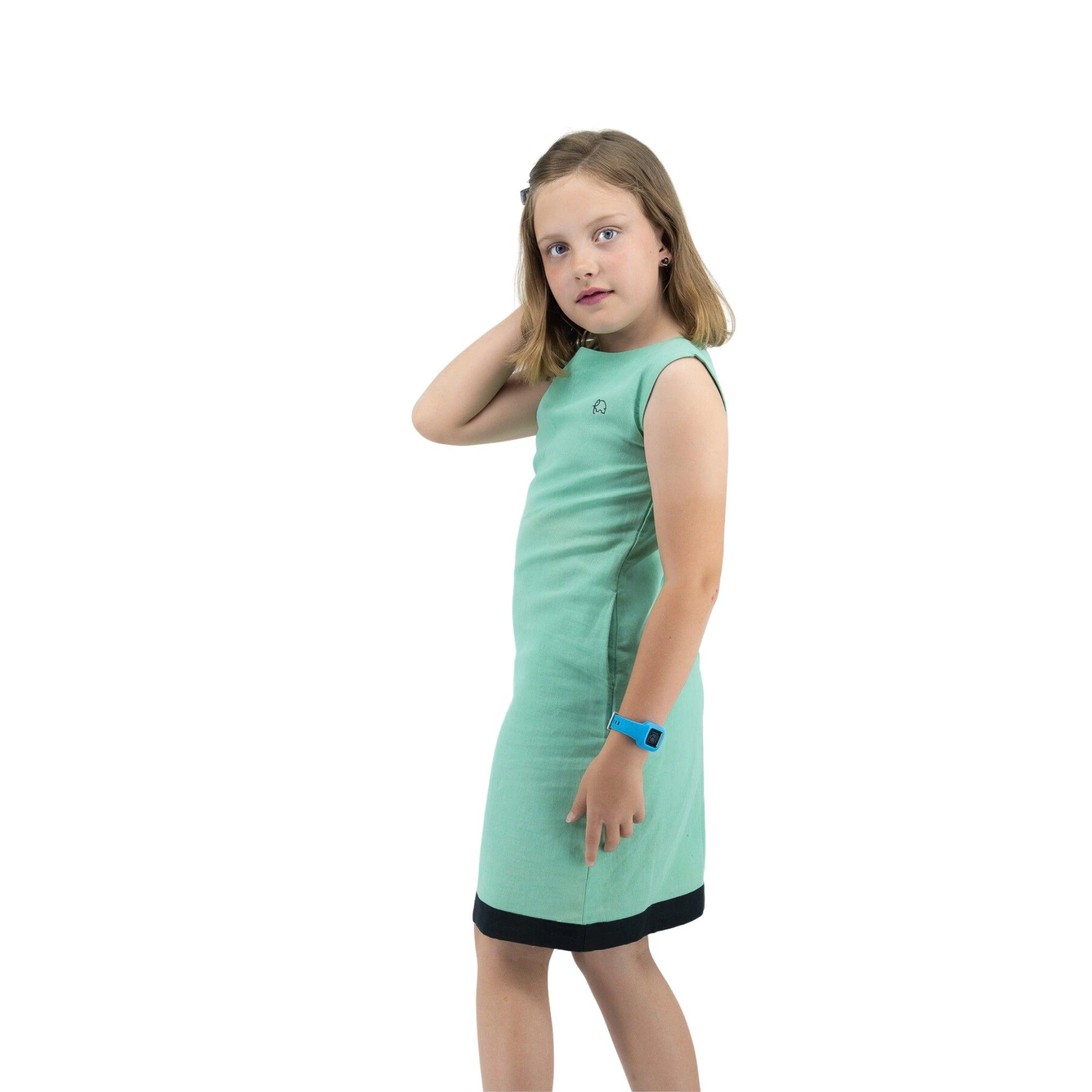 Young girl in a Karee Neptune green Linen Cotton Round Neck Frock for Kids with a smartwatch, standing and looking to the side, isolated on a white background.