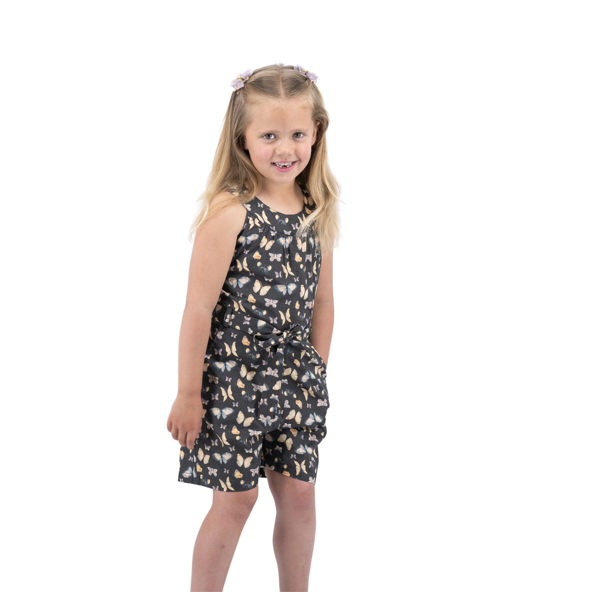 Young girl in a Karee Pirate Black Adventure-ready Cotton Play Suit for girls smiling and looking to the side against a white background.