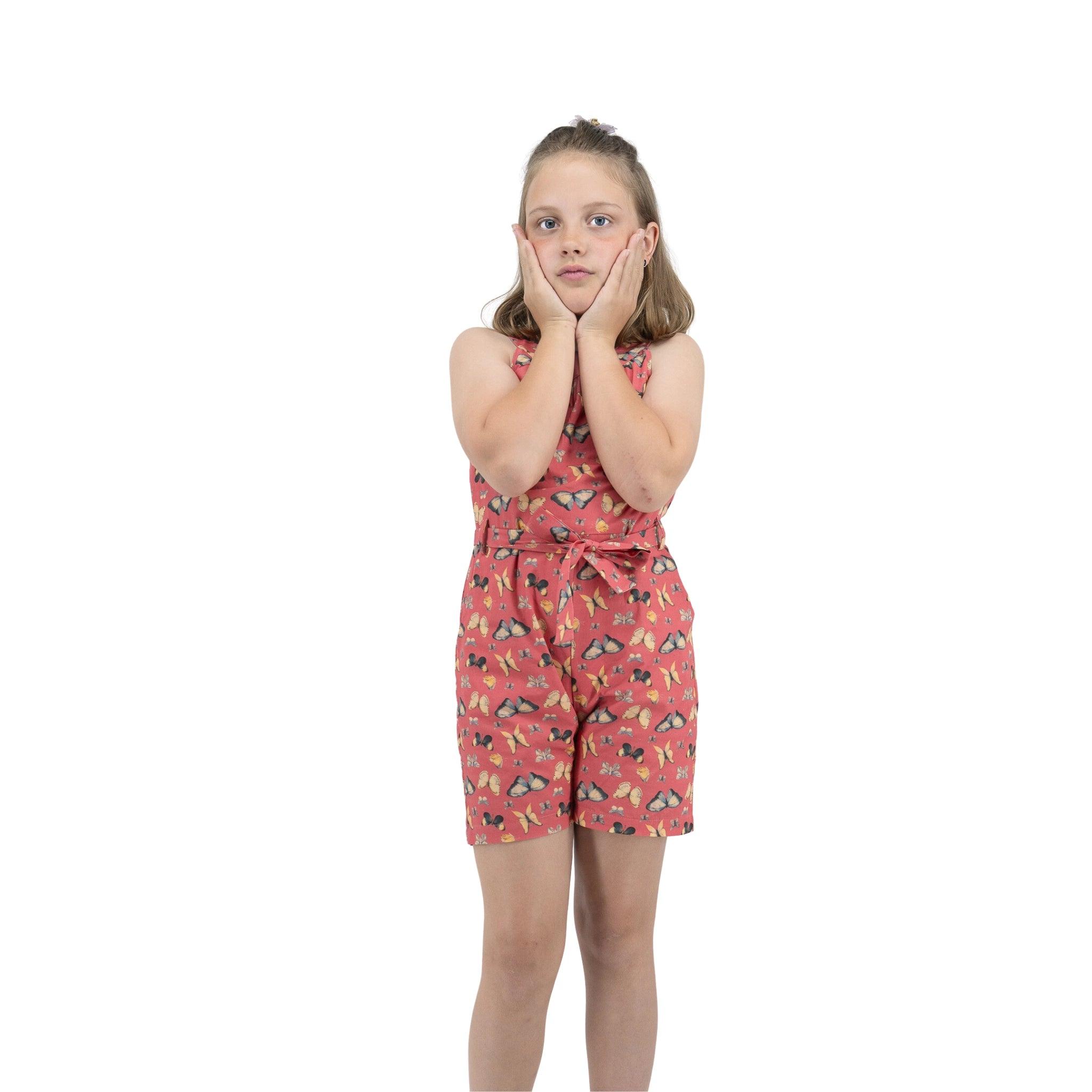 Young girl in a Ruby Trek Cotton Romper by Karee standing with hands on cheeks looking thoughtful, isolated on white background.