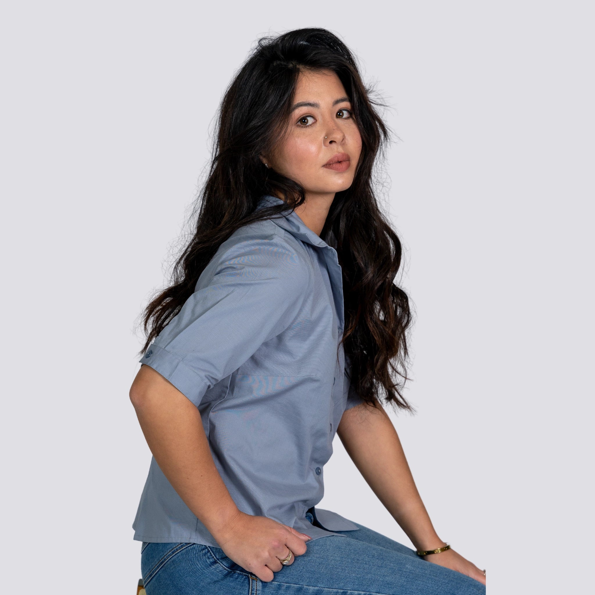 Woman in a Karee Grey Mist Linen Shirt posing sideways with a subtle glance towards the camera, set against a plain white background.