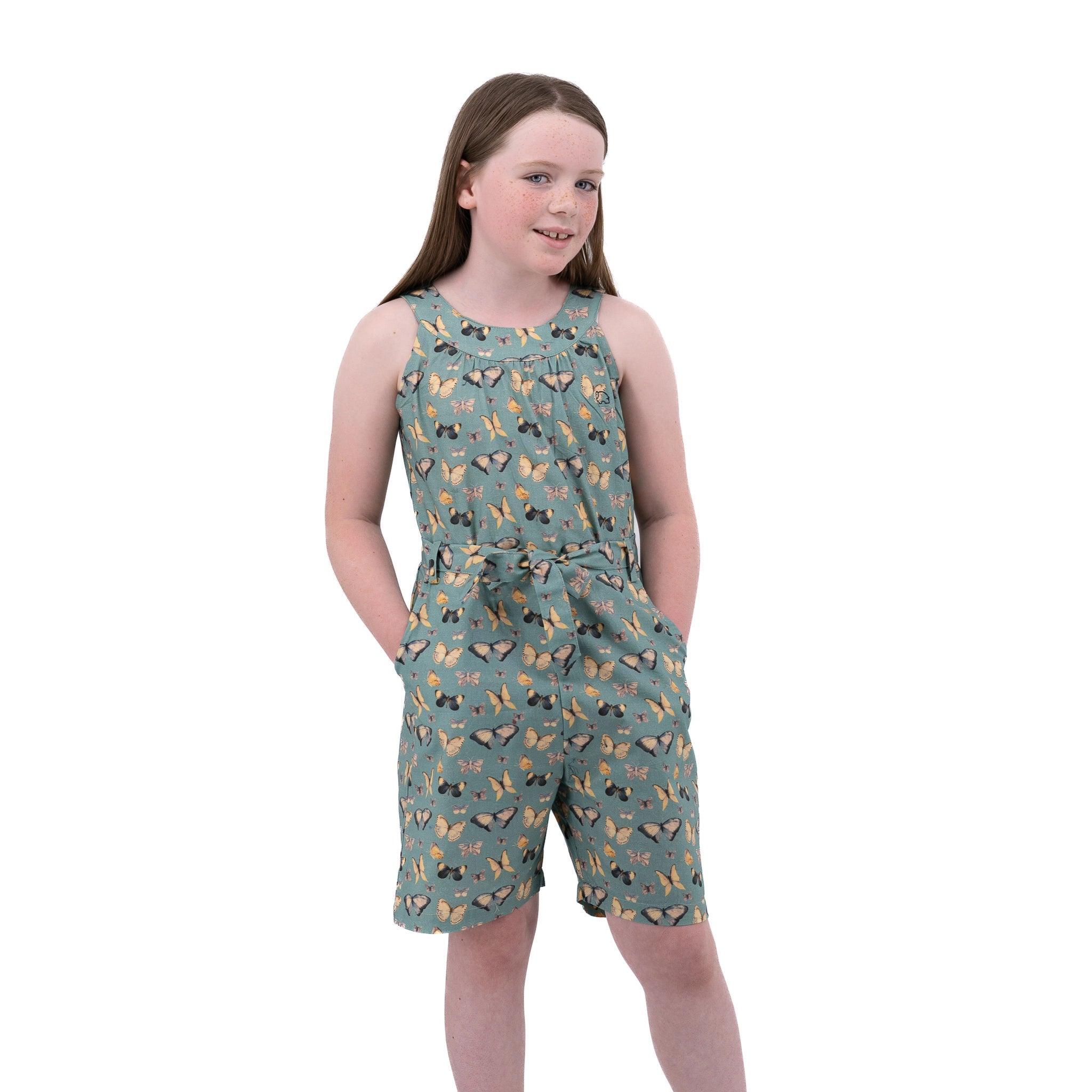 Young girl in a Karee Blue Surf Adventure-ready Cotton Play Suit standing against a white background, looking to the side with a subtle smile.