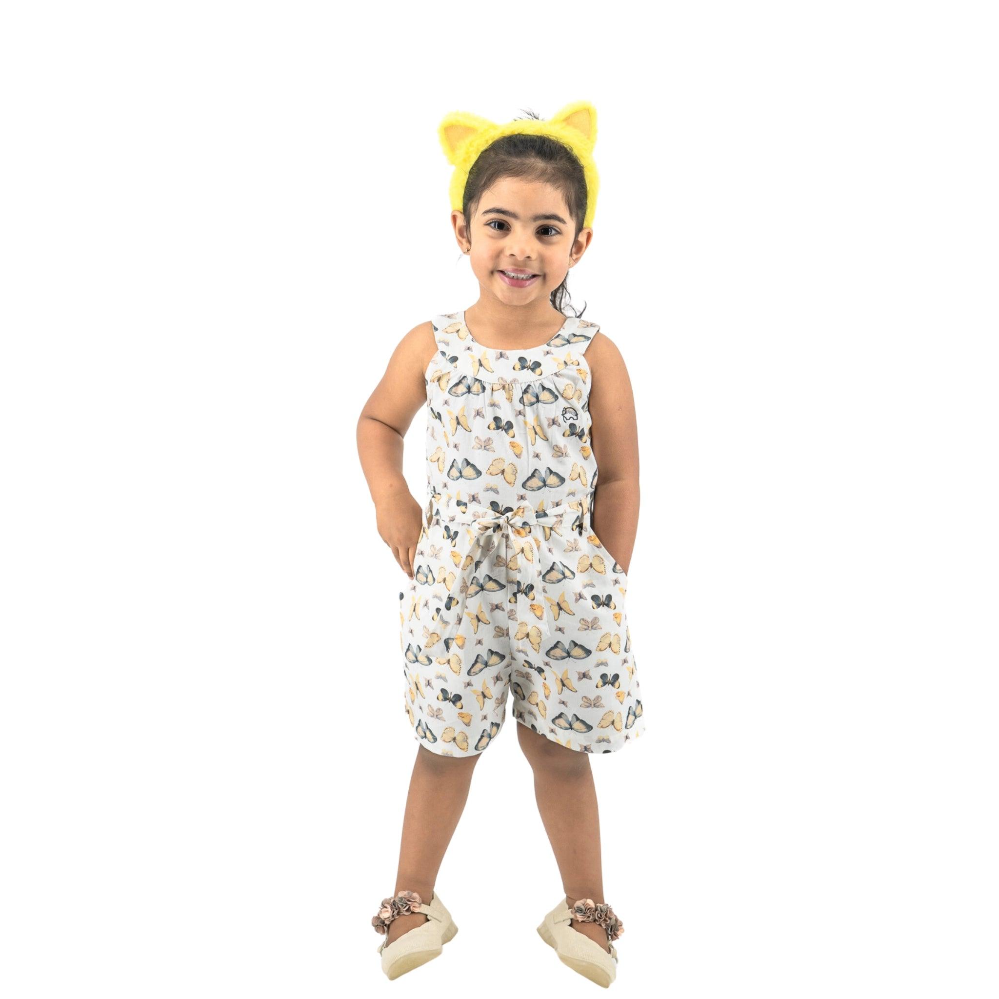 Young girl in a Karee White Adventure-Ready Cotton Play Suit and yellow hairband standing and smiling against a white background.